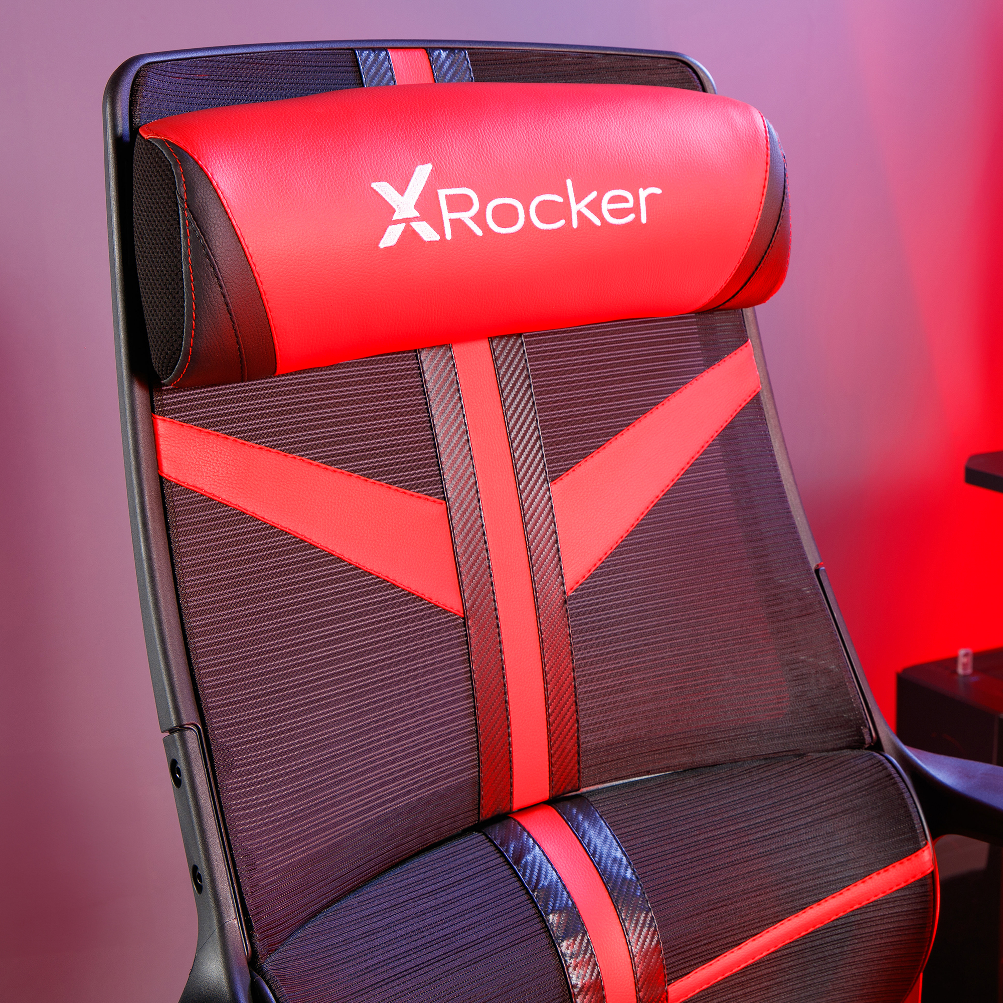Ein rot-schwarzer Gaming-Stuhl mit dem X Rocker-Logo auf der Kopfstütze. Der Hintergrund ist rot beleuchtet.