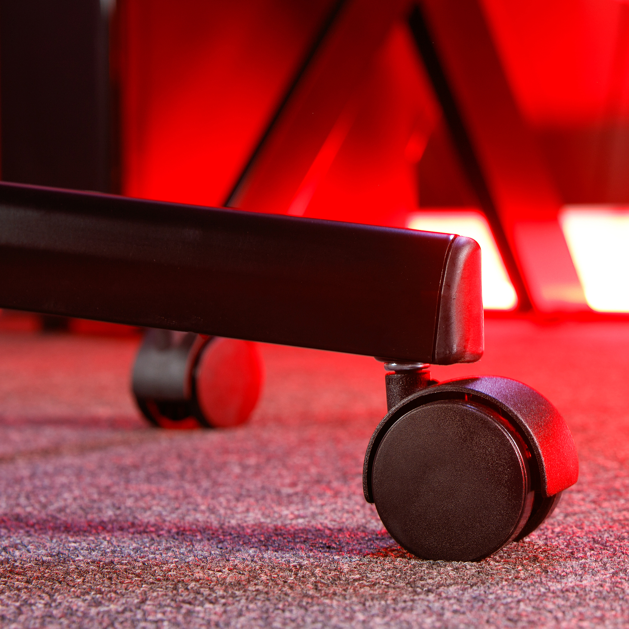 Nahaufnahme der schwarzen Räder eines Gaming-Stuhls auf einem Teppichboden. Rote Beleuchtung.