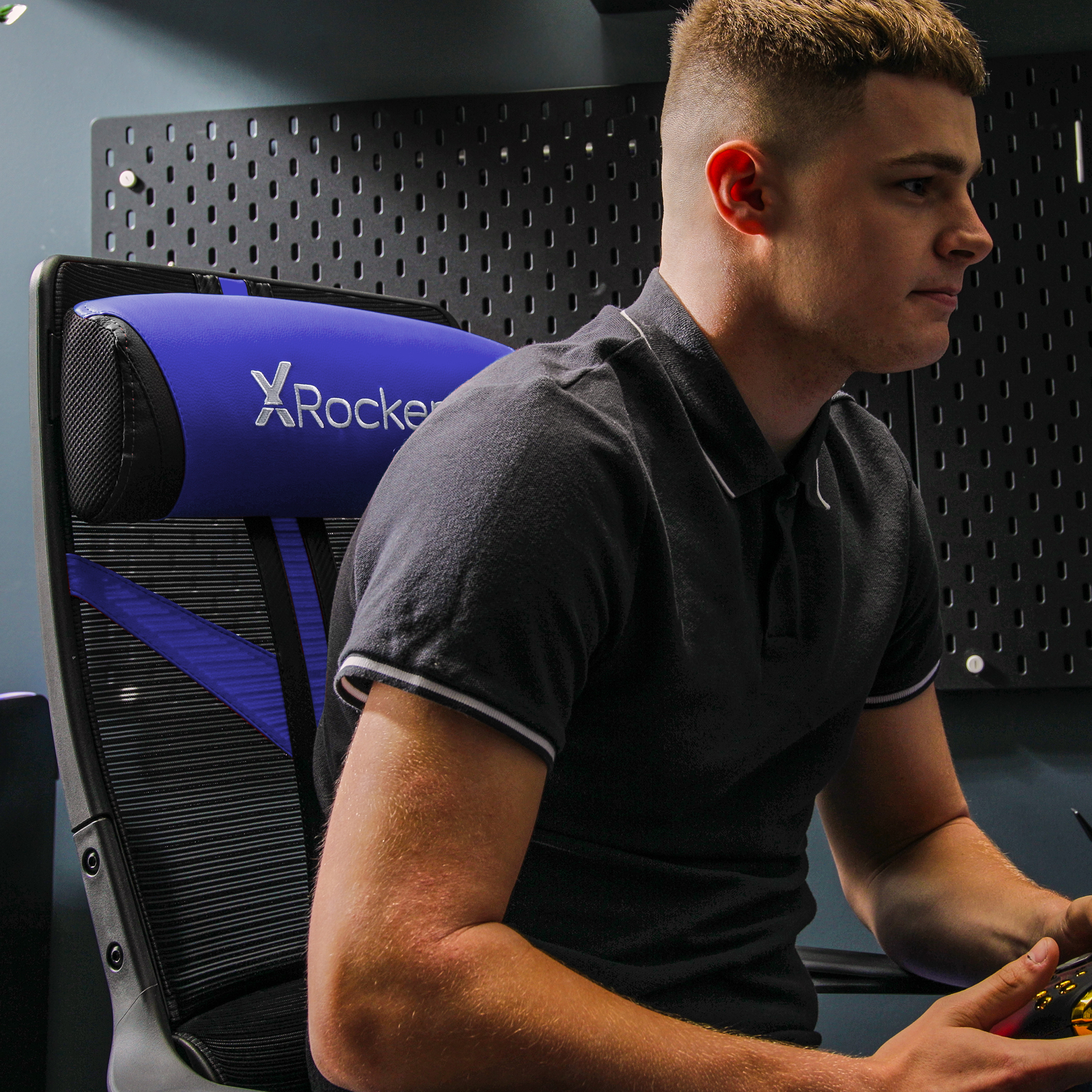 Ein Mann in einem schwarzen Poloshirt sitzt in einem Gaming-Stuhl und schaut auf einen Bildschirm, mit X-Rocker-Kopfstütze.