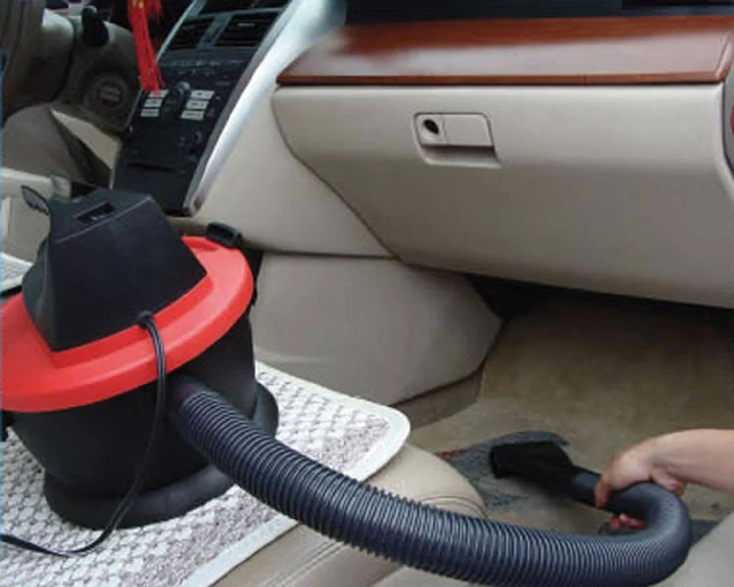 Un interno auto in fase di aspirazione con un aspirapolvere portatile. L'aspirapolvere è nero e rosso.