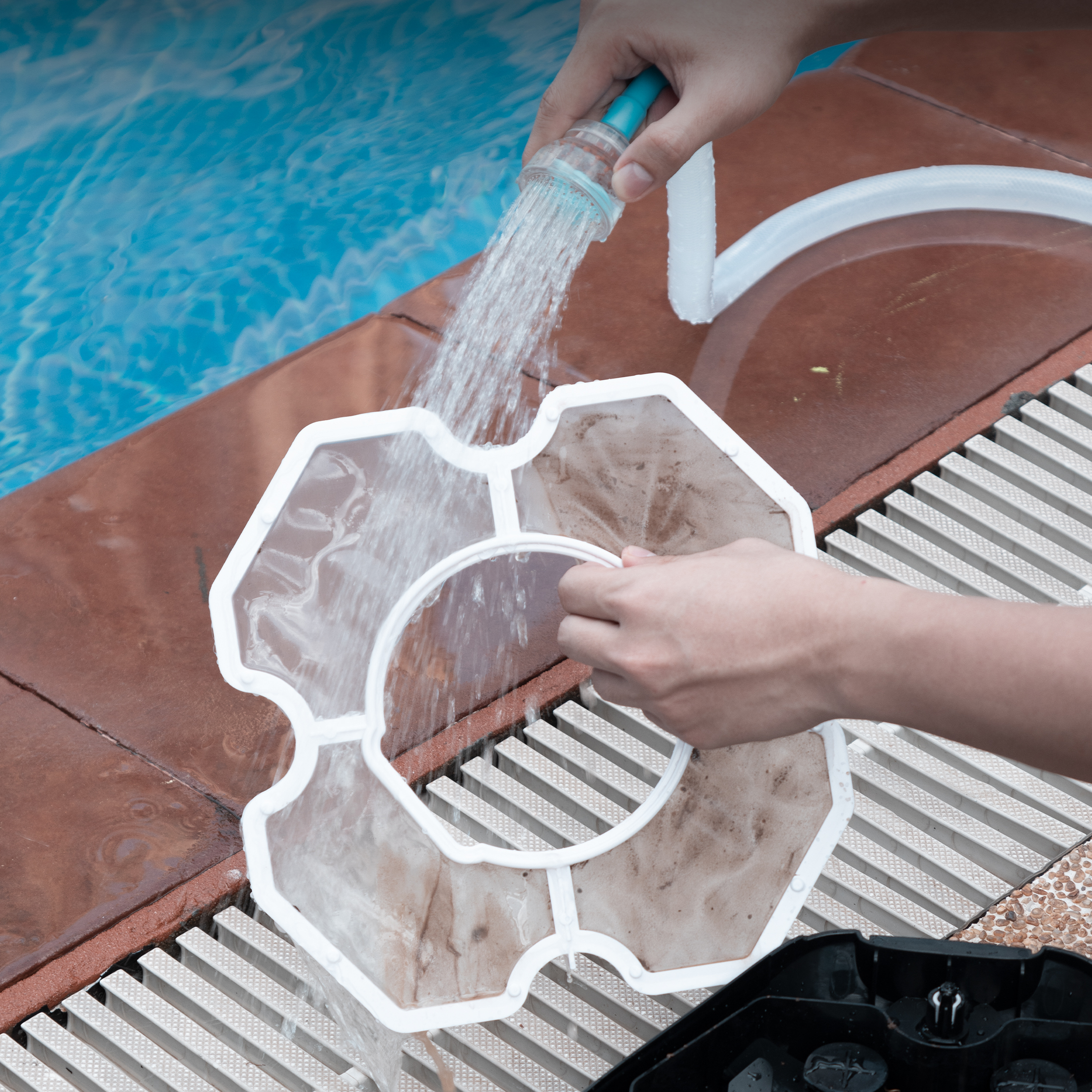 Mani che puliscono un filtro per piscina con un tubo, l'acqua scorre. Piscina sullo sfondo.