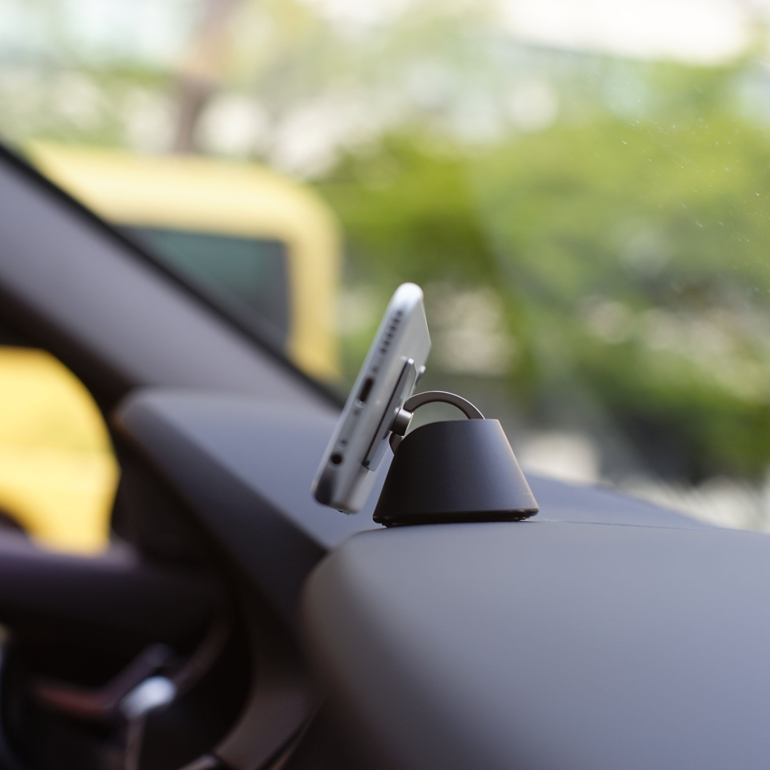 Kfz-Telefonhalterung mit angebrachtem Telefon, montiert auf dem Armaturenbrett, gelbes Auto sichtbar.