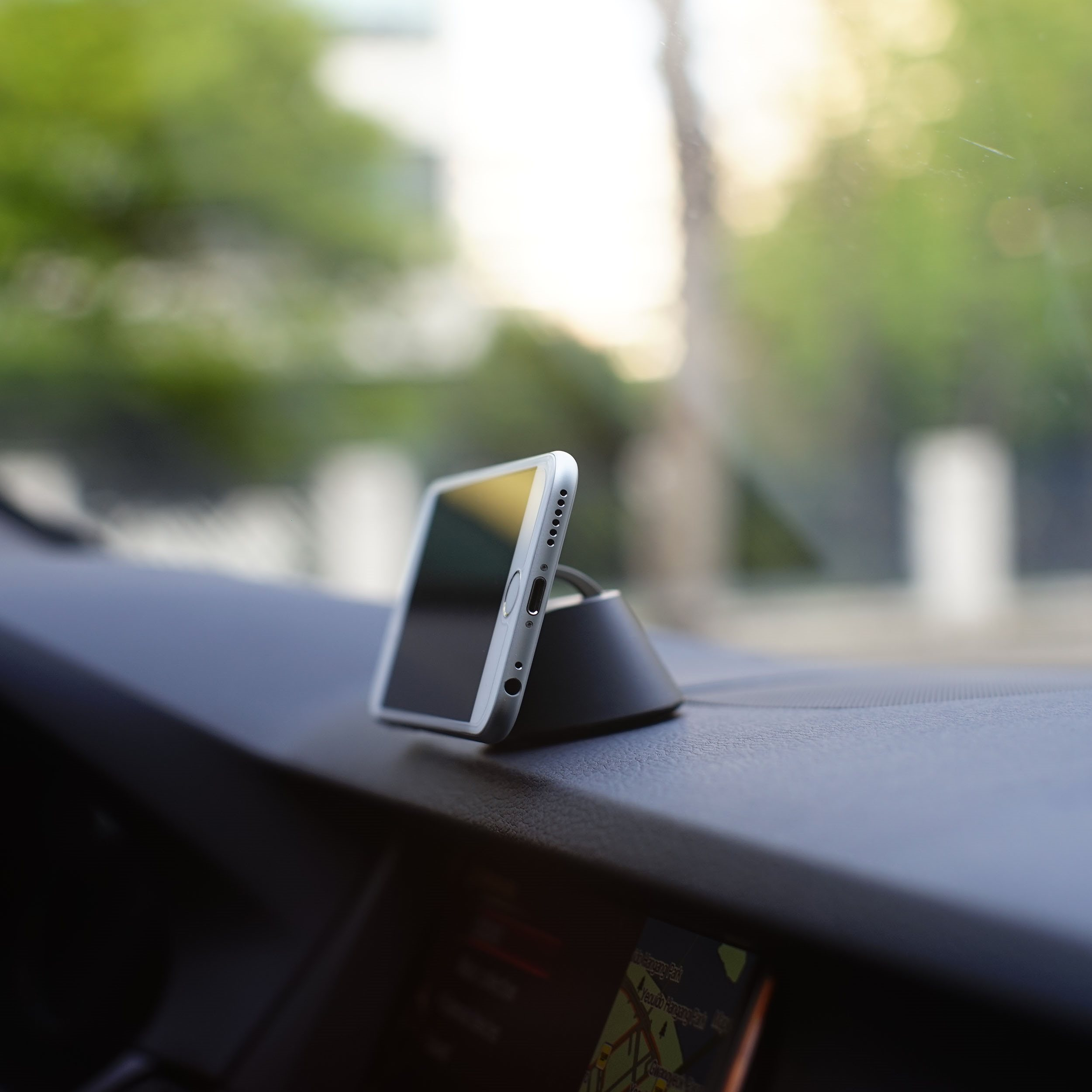 Ein weißes Telefon auf einer schwarzen Telefonhalterung in einem Auto. Armaturenbrett und unscharfer Hintergrund.