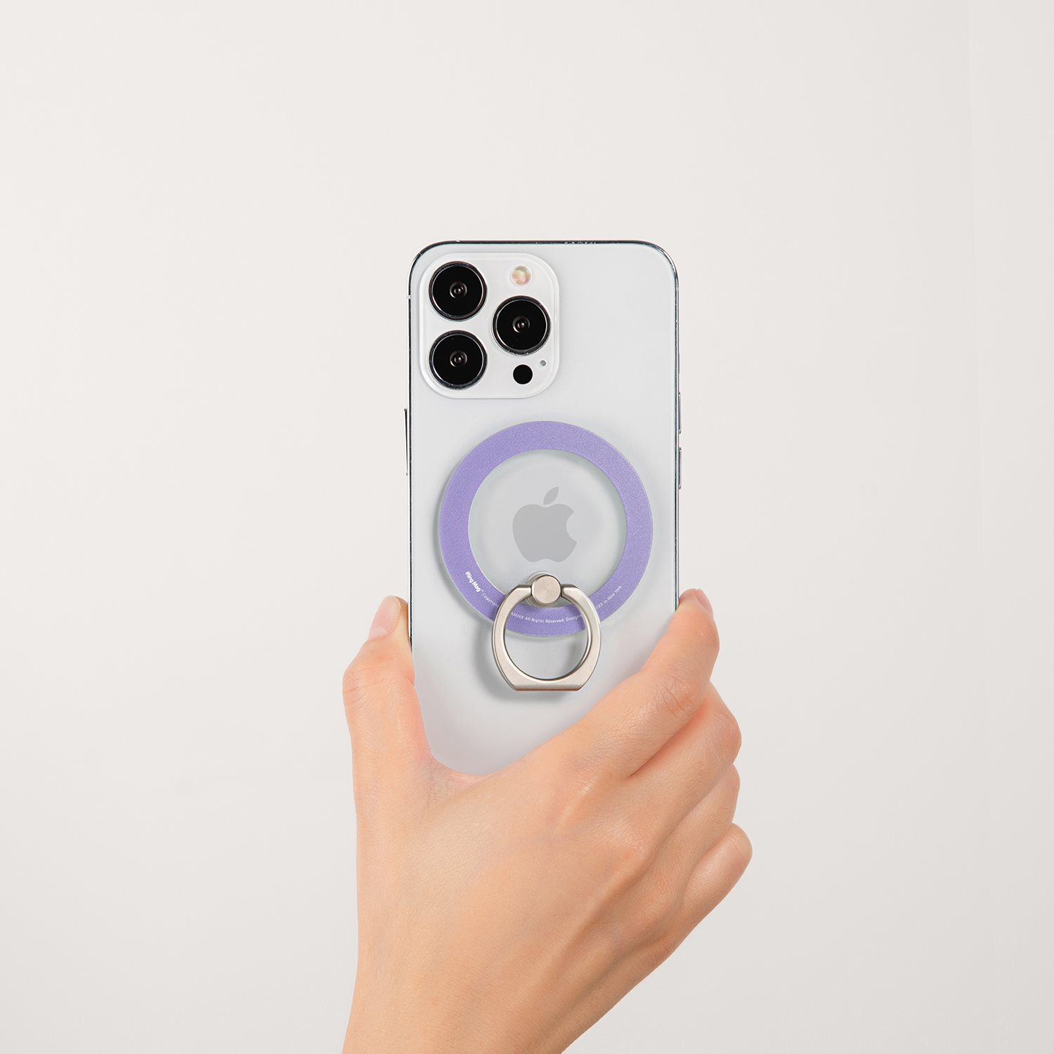Eine Hand hält ein weißes iPhone mit einem lila Ring und einem Metallringhalter. Der Hintergrund ist weiß.