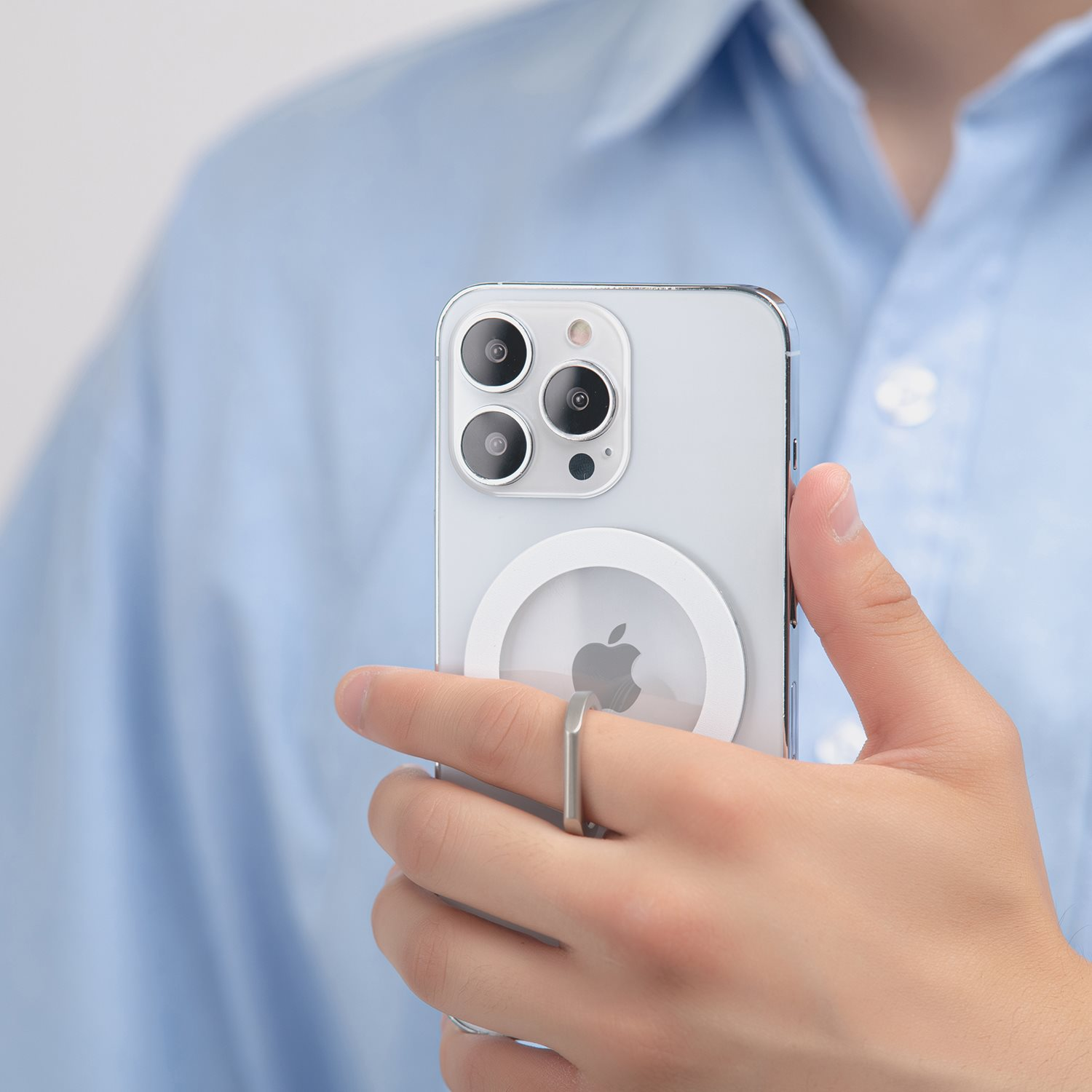 Eine Hand hält ein weißes Telefon mit einem Ringhalter. Hellblaues Hemd im Hintergrund.