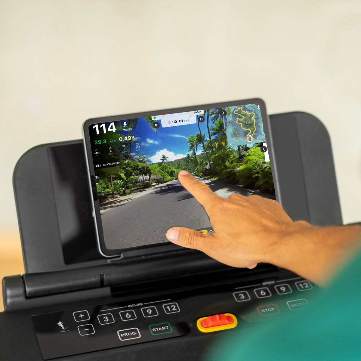 Die Hand einer Person berührt einen Tablet-Bildschirm auf einem Laufband. Der Bildschirm zeigt eine virtuelle Landschaft.