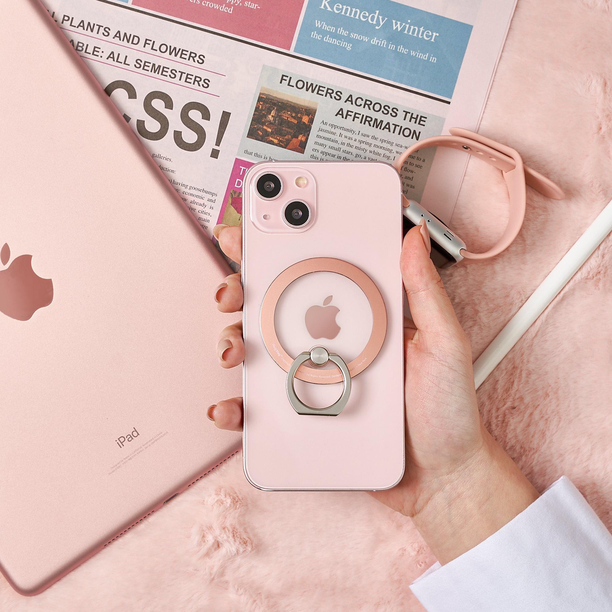 Ein rosa iPhone mit Ringhalter, ein rosa iPad und Zeitung. Eine Hand hält das Telefon.