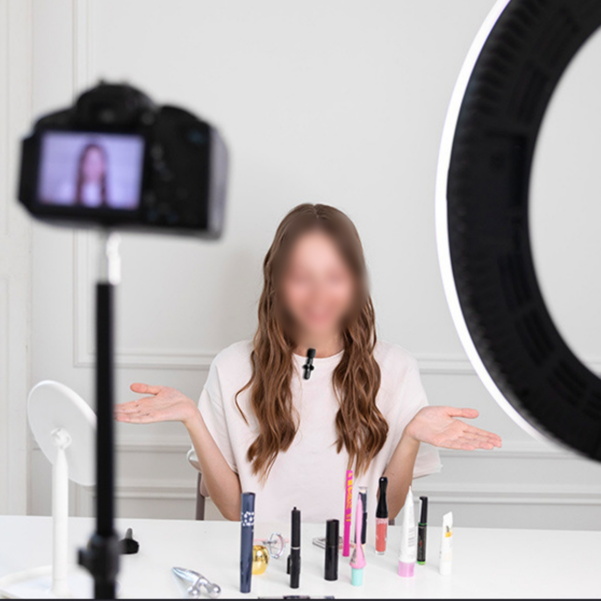 Frau vor Kamera, verschwommenes Gesicht. Make-up-Produkte und Ringlicht auf dem Tisch.