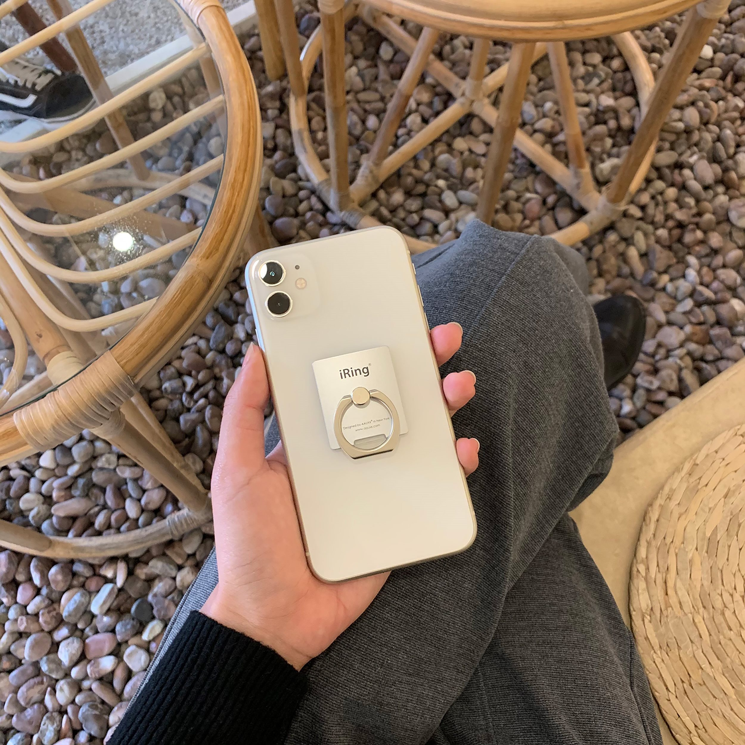Die Hand einer Person, die ein weißes Telefon mit einem iRing-Aufsatz hält, mit einem Korbstuhl.