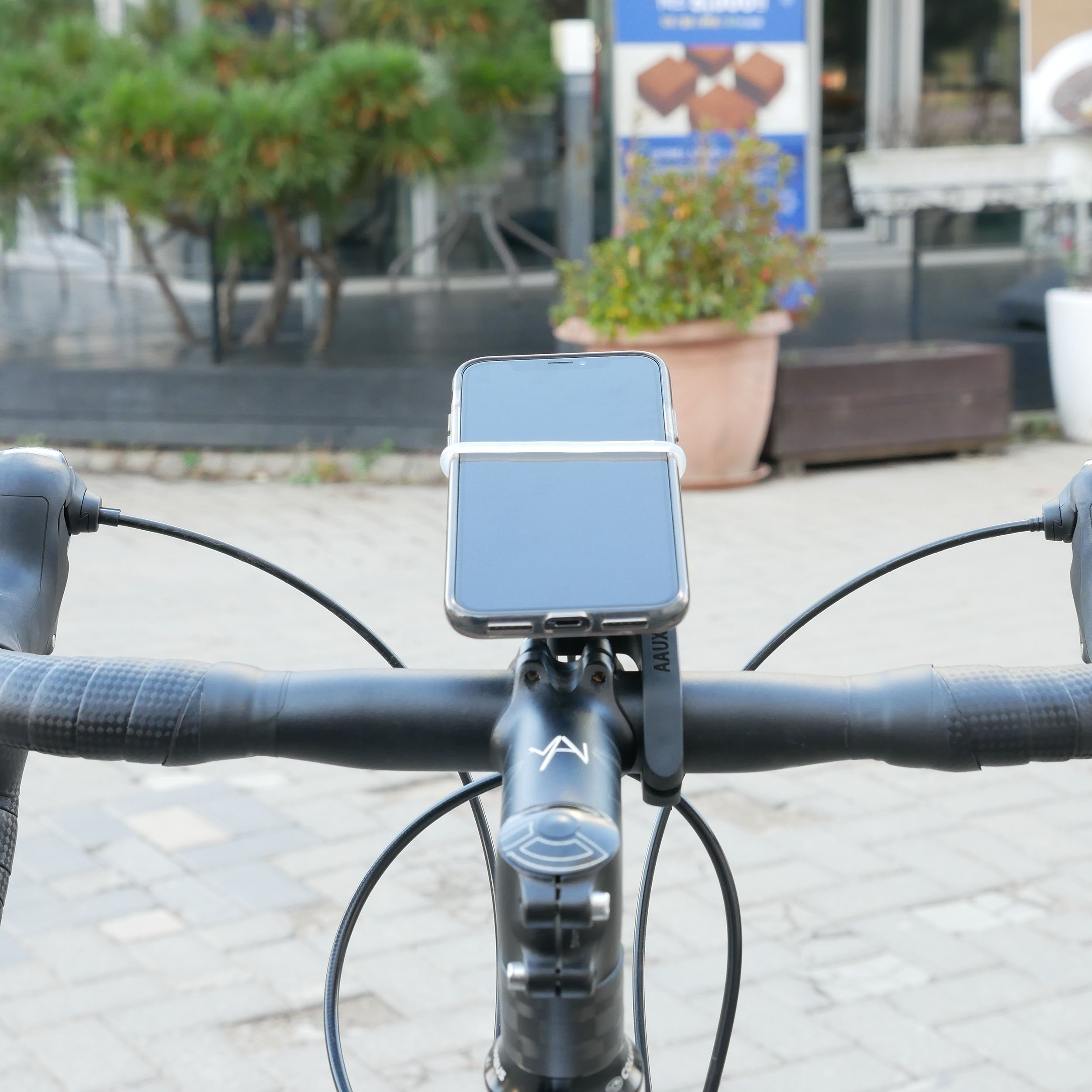 Smartphone an Fahrradlenker montiert. Schwarzes Telefon in weißem Halter. Draußen.