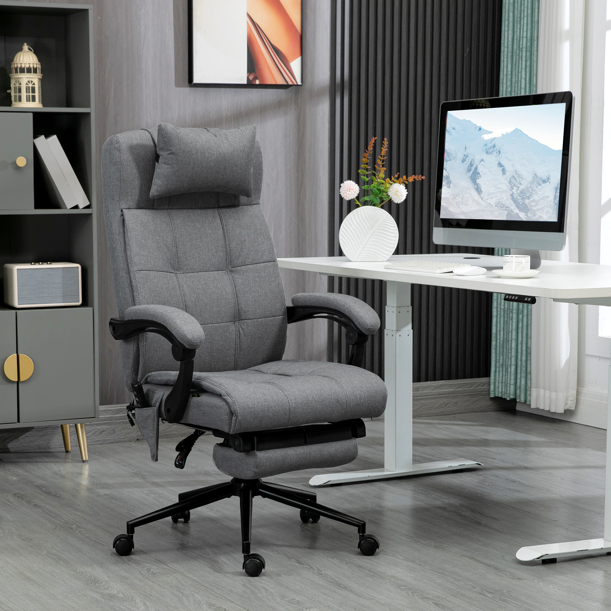 Sedia da ufficio ergonomica grigia con poggiatesta, braccioli e poggiapiedi, vicino a una scrivania bianca e un computer.