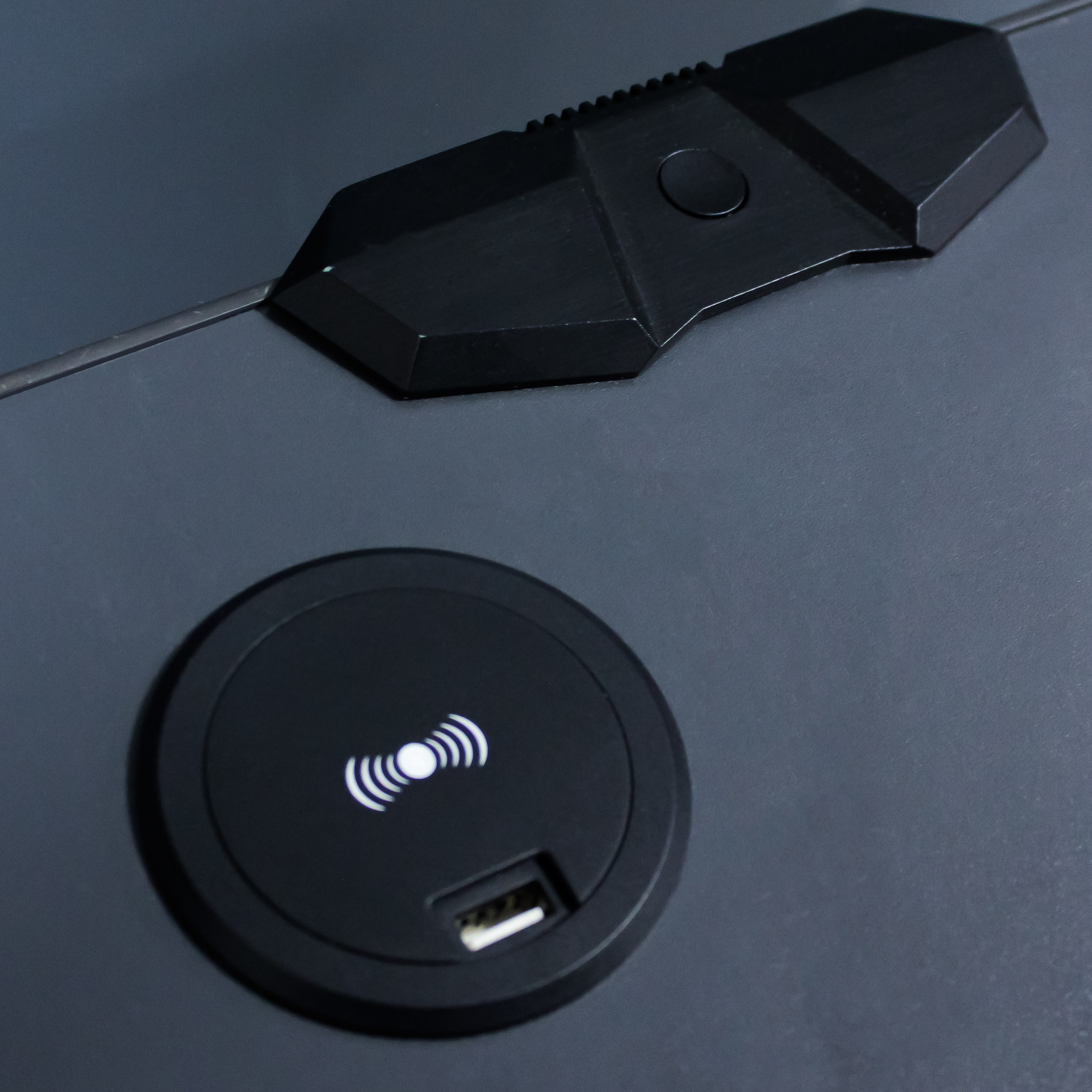 Ein schwarzes kabelloses Ladepad mit USB-Anschluss und weißer Ladeanzeige auf grauer Oberfläche.