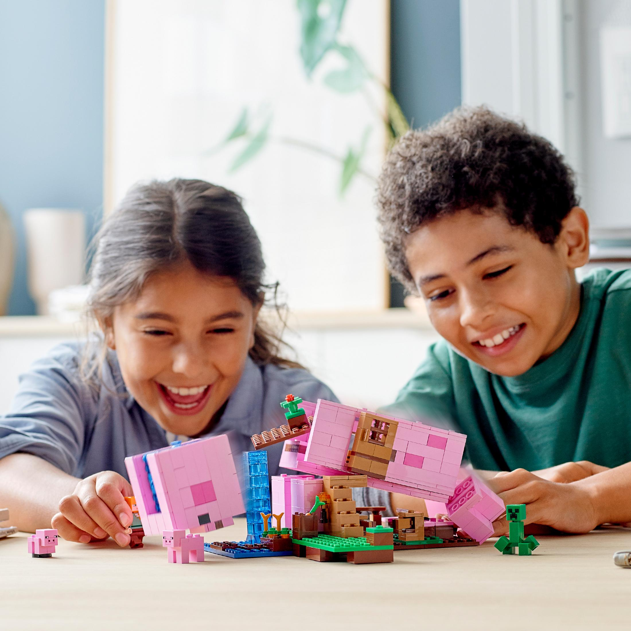 Due bambini giocano con un set Lego Minecraft su un tavolo di legno, sorridendo e ridendo.