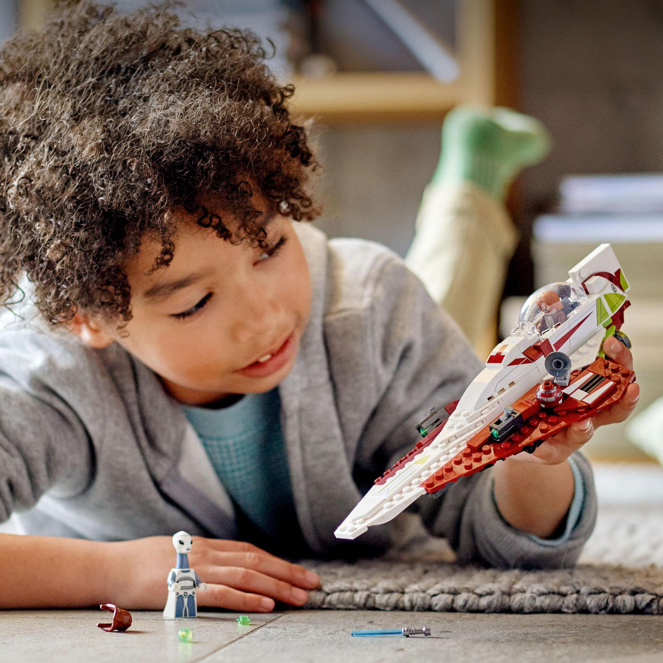Chłopiec trzyma statek LEGO Star Wars, z figurkami i przedmiotami na stole.