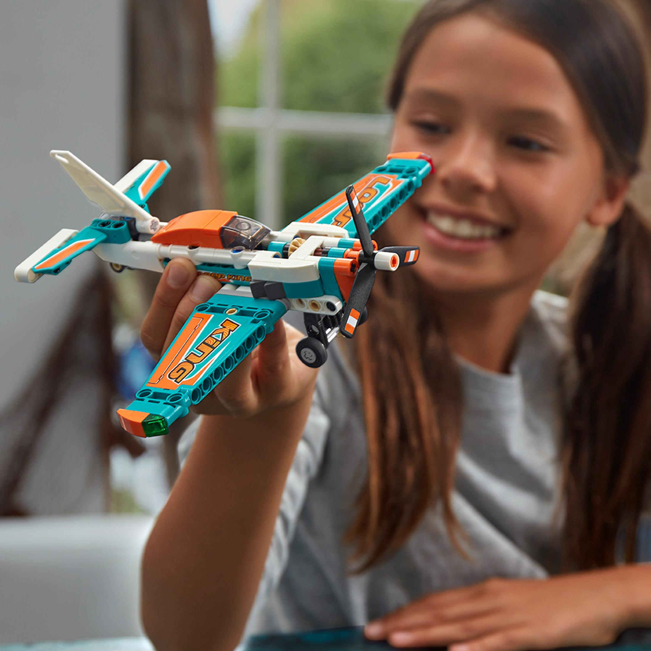 Ein Mädchen hält ein LEGO-Flugzeugmodell mit orangefarbenen und tealfarbenen Akzenten.
