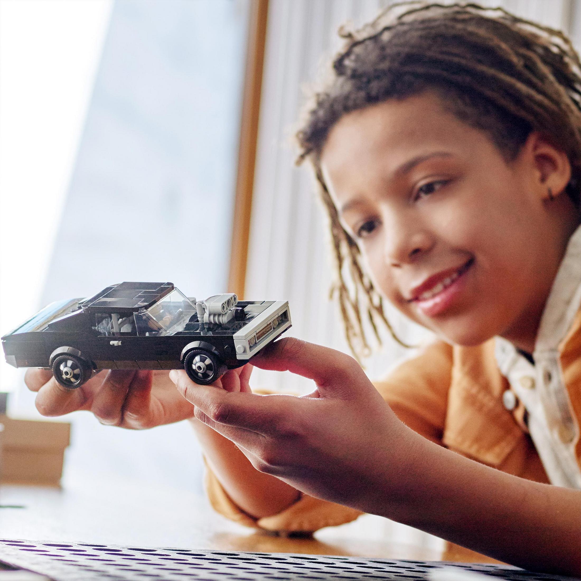 Chłopiec trzyma czarny samochodzik, uśmiechając się. Samochód ma biały dach.