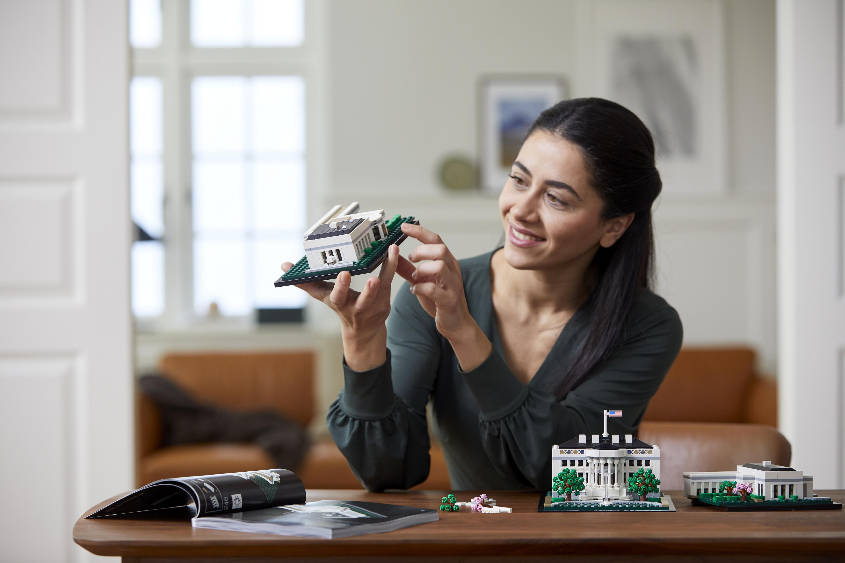 Kobieta składa model Lego budynku, trzymając w ręku element.