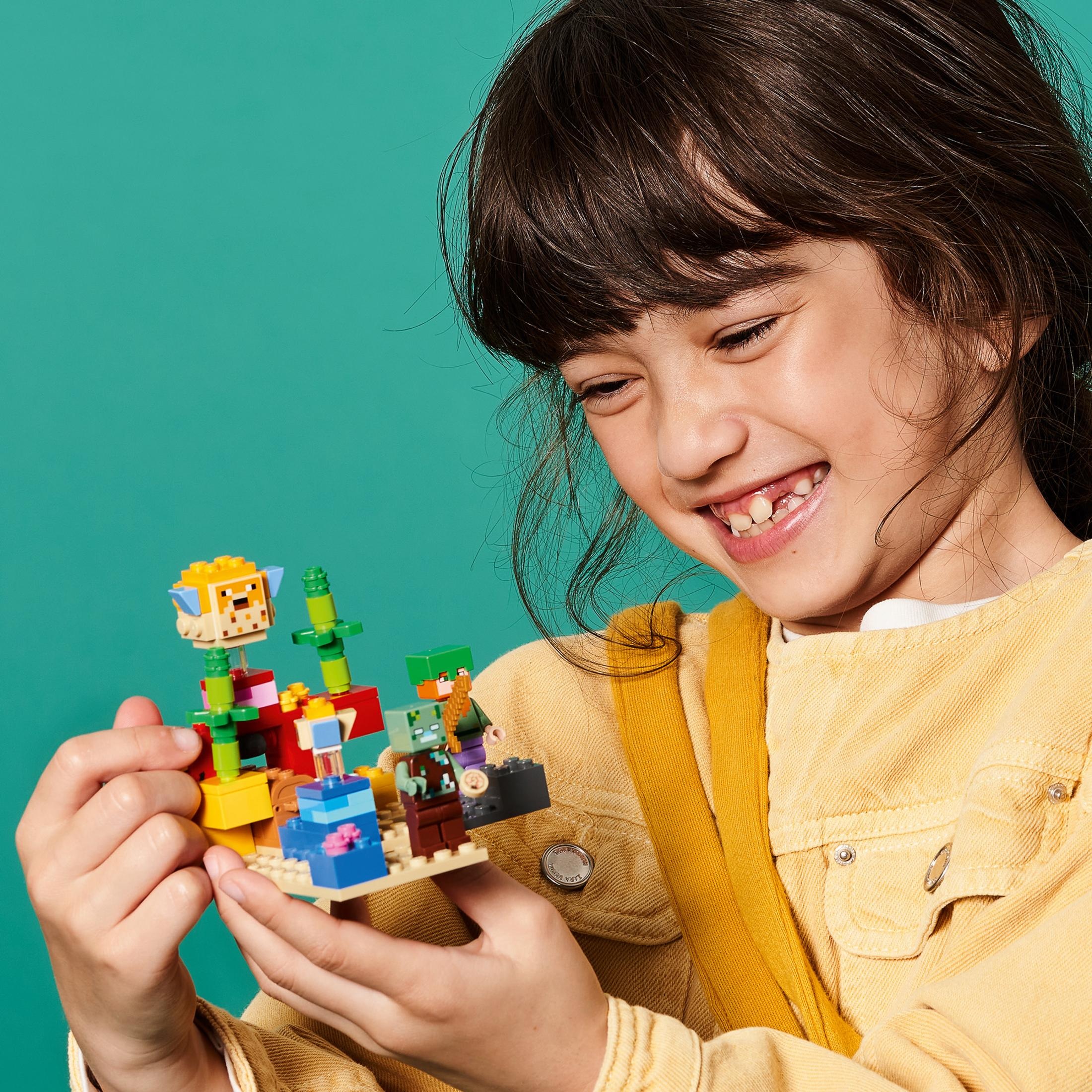 Bambina che gioca con il set Lego Minecraft. Blocchi e figure colorate. Sfondo turchese.
