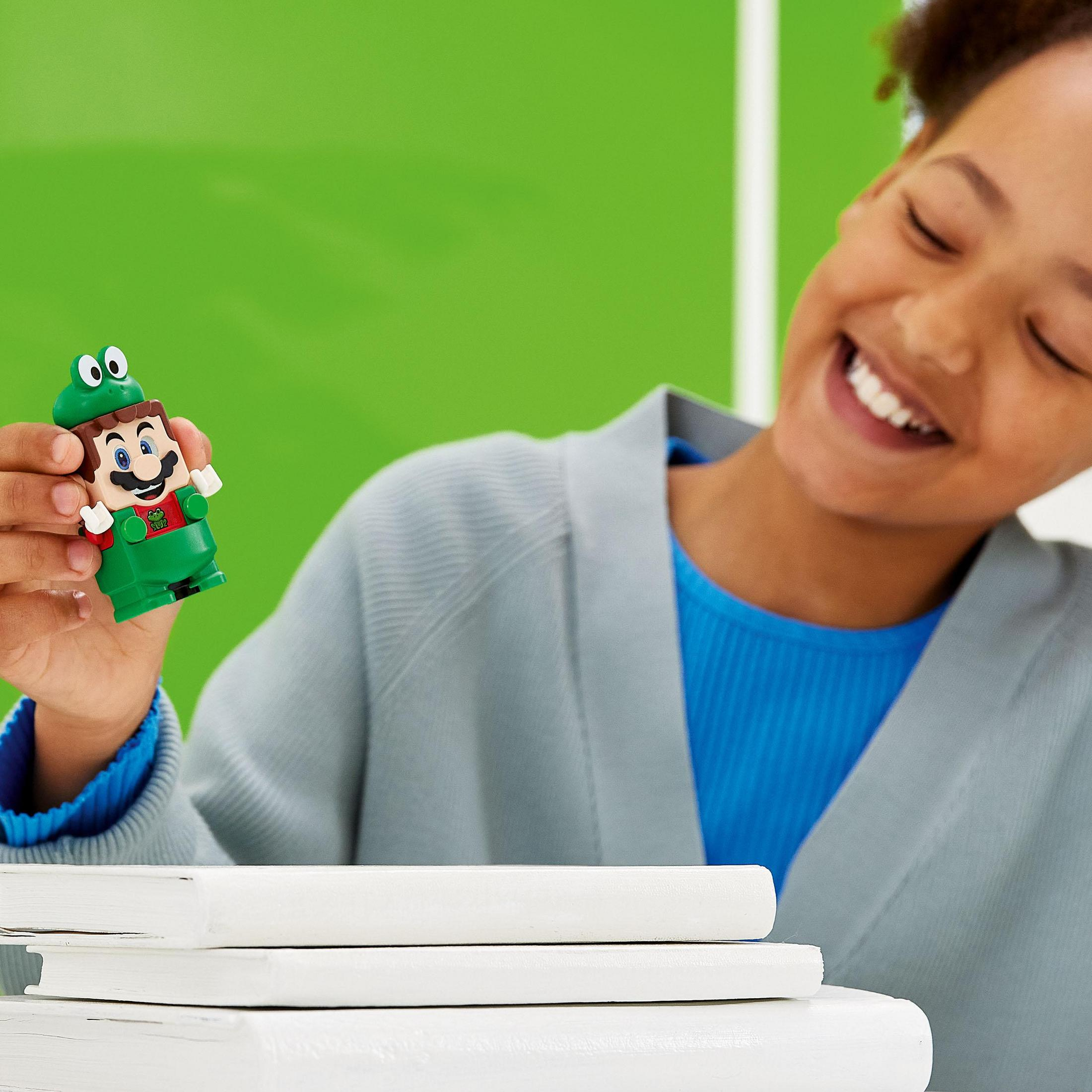 Ein junges Mädchen lächelt, hält eine Lego Luigi-Figur, grüner Hintergrund und Bücher.