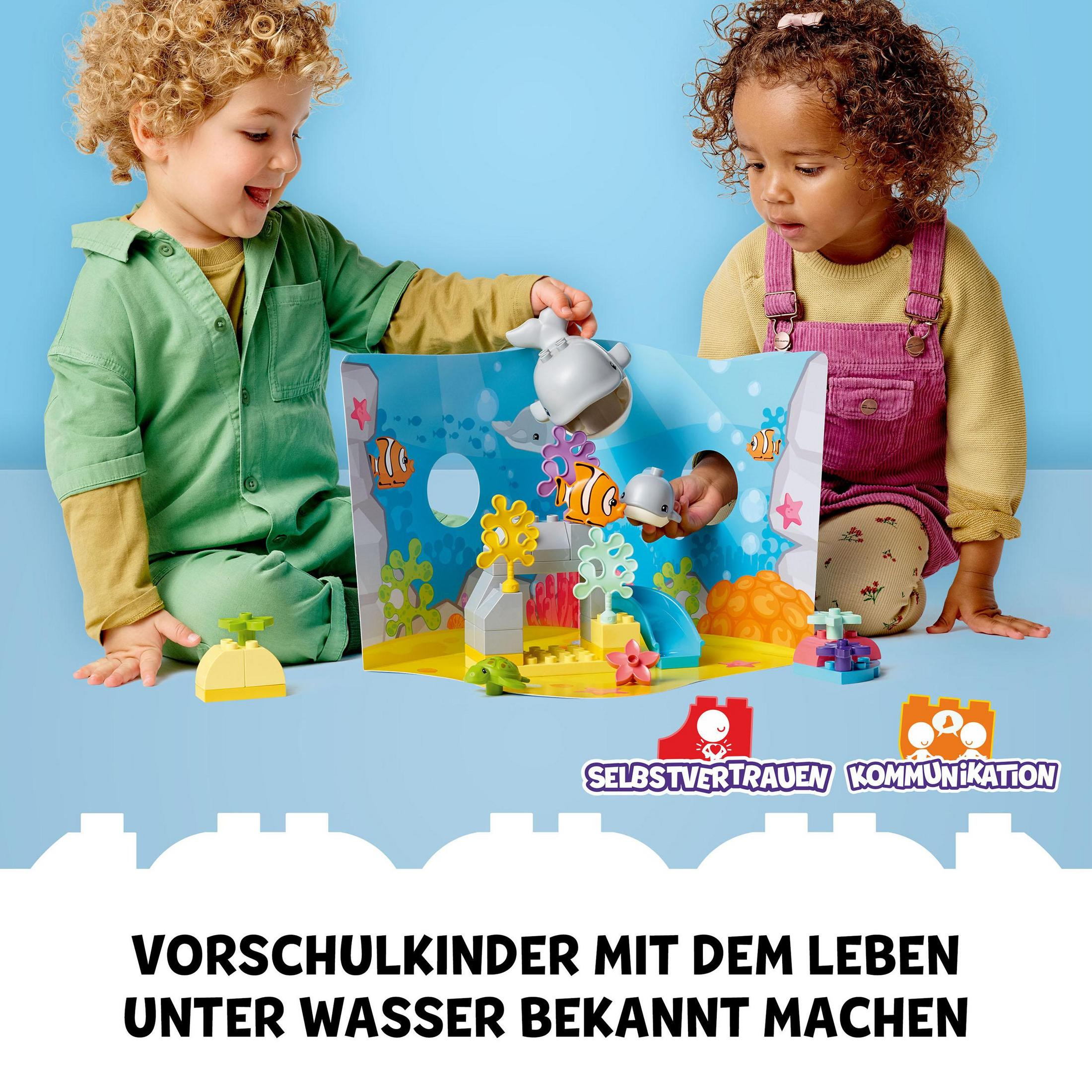 Zwei Kinder spielen mit Lego. Eine Meereslandschaft mit Fischen und einem Hai ist sichtbar.