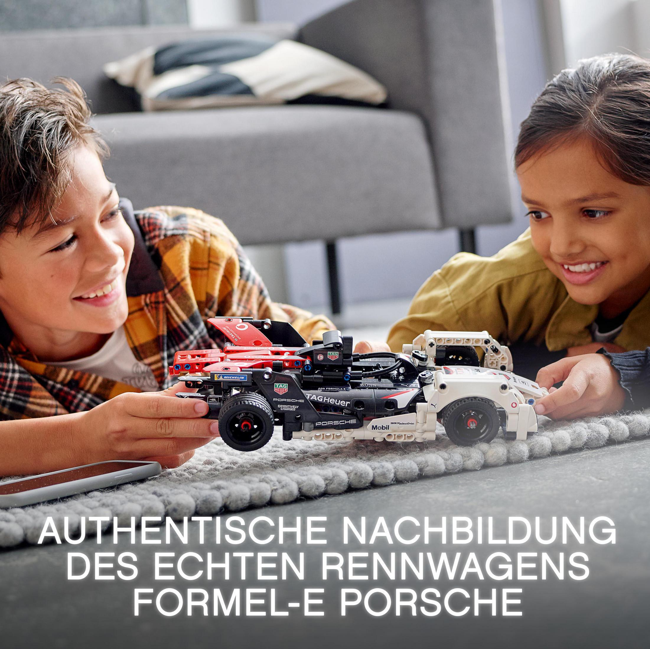 Zwei Kinder spielen mit einem Lego-Rennwagen. Das Auto ist schwarz, rot und weiß. Im Hintergrund ist eine graue Couch.