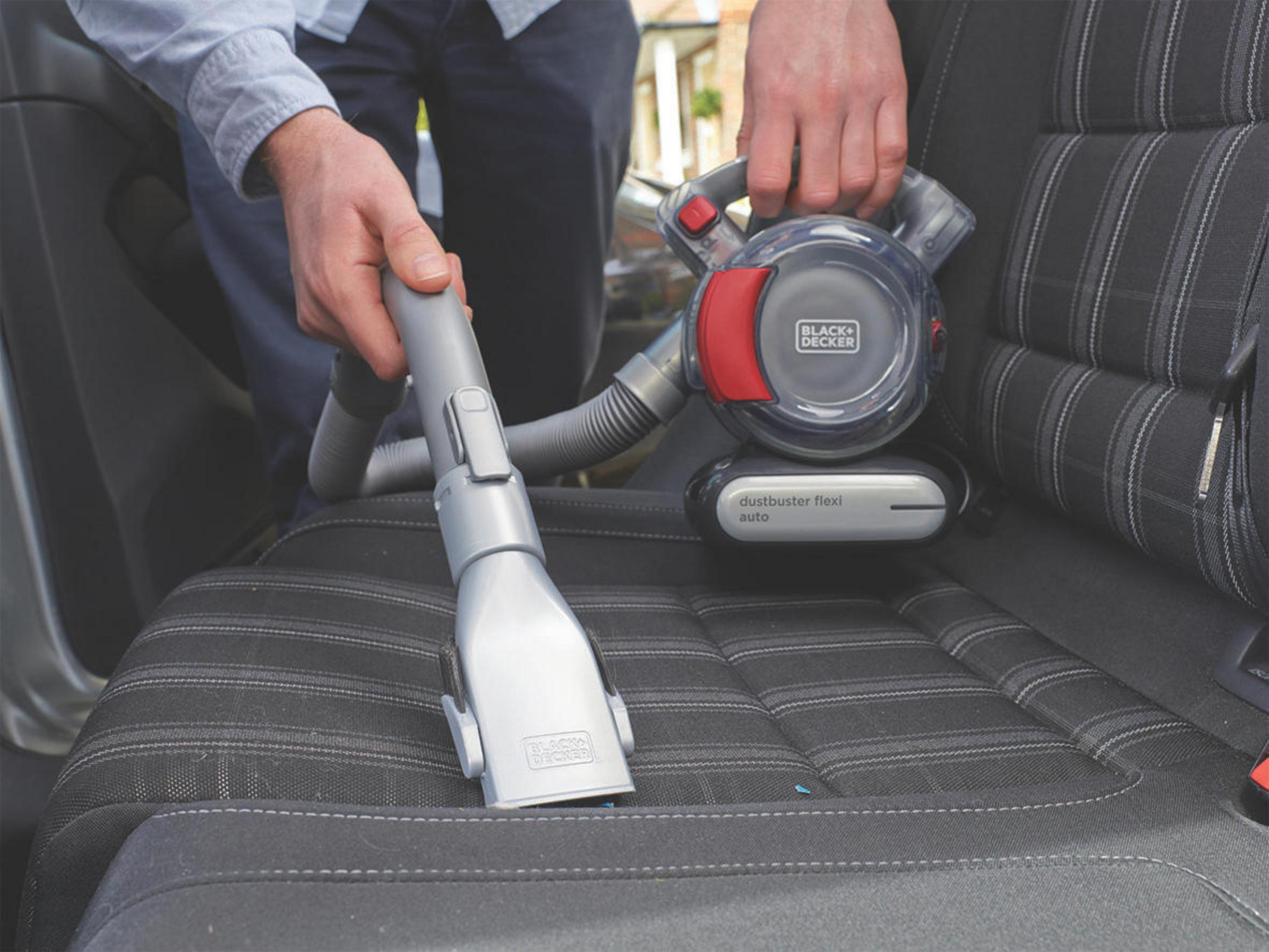 Osoba używająca czarno-czerwonego odkurzacza Black+Decker na siedzeniu samochodu.