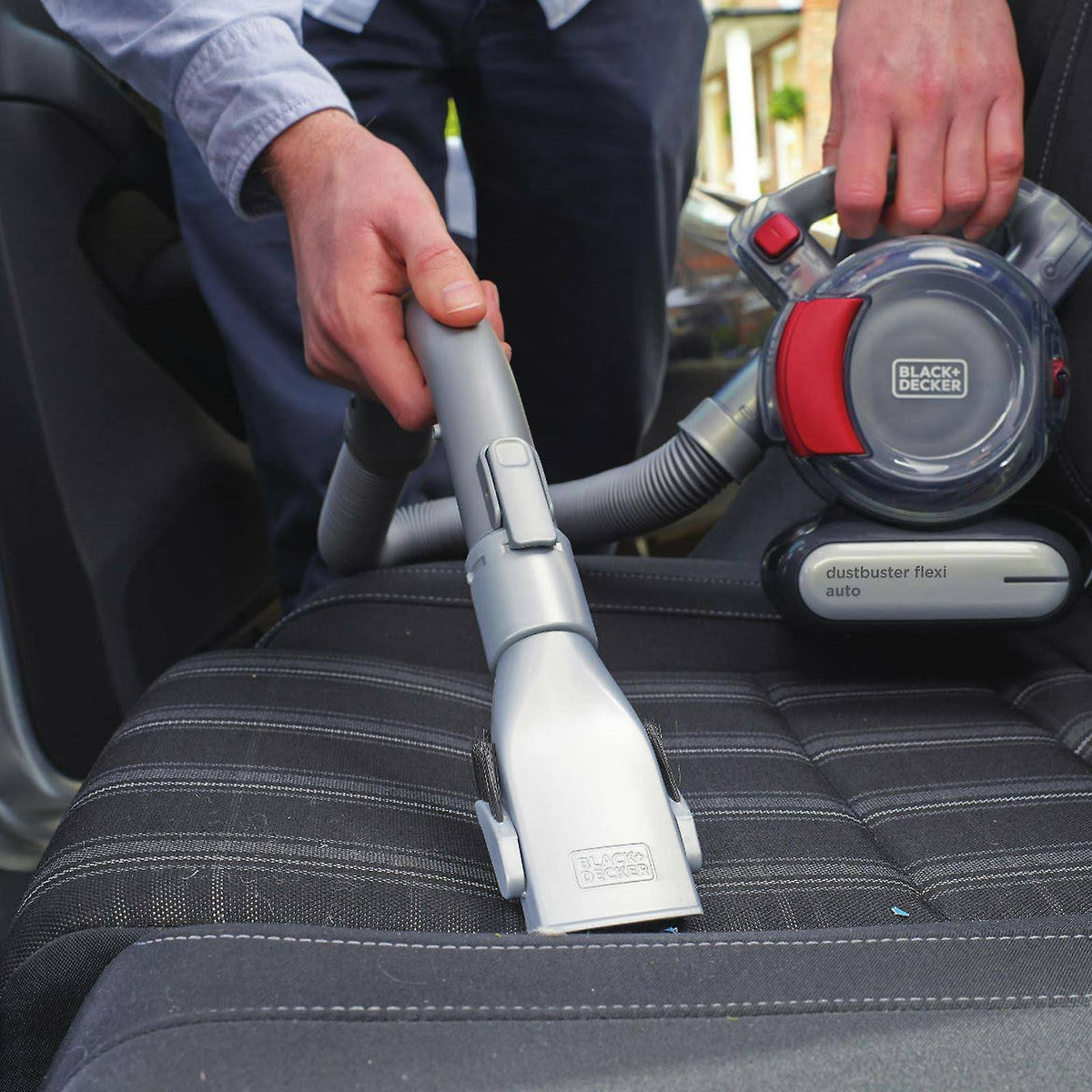 Osoba odkurza siedzenie samochodu odkurzaczem Black+Decker.
