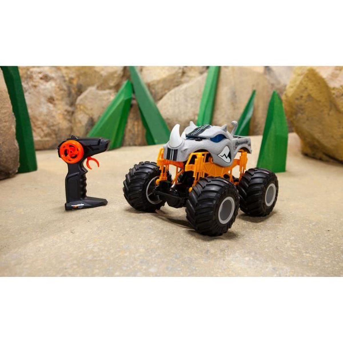 RC-Monstertruck mit Controller. Beiger Boden, grüne Bäume, felsiger Hintergrund.