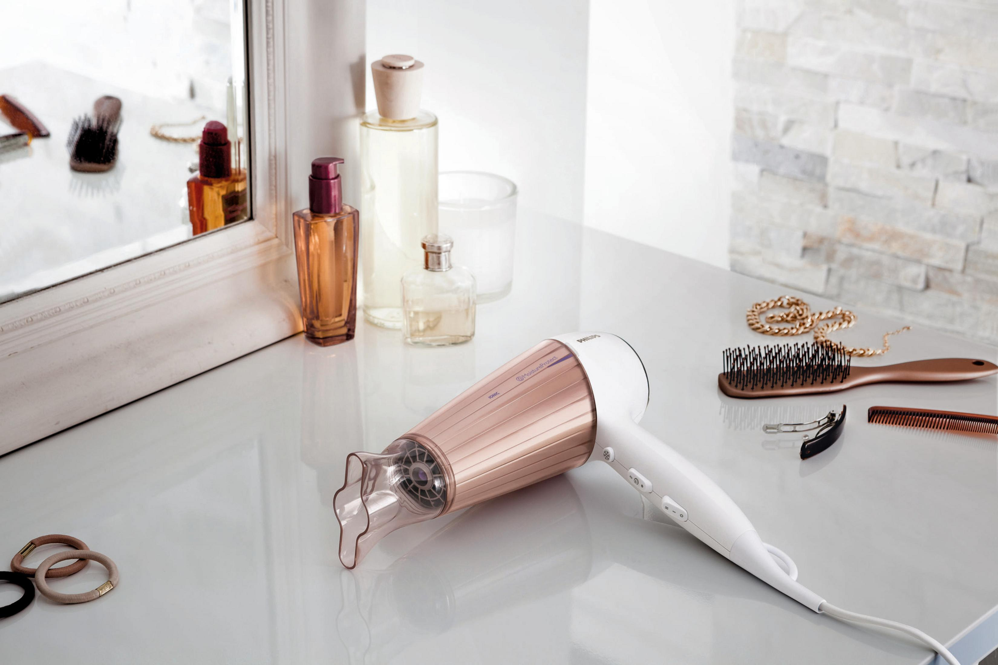 Secador de pelo, accesorios y espejo en una mesa blanca. Secador de pelo oro rosa y fondo blanco.