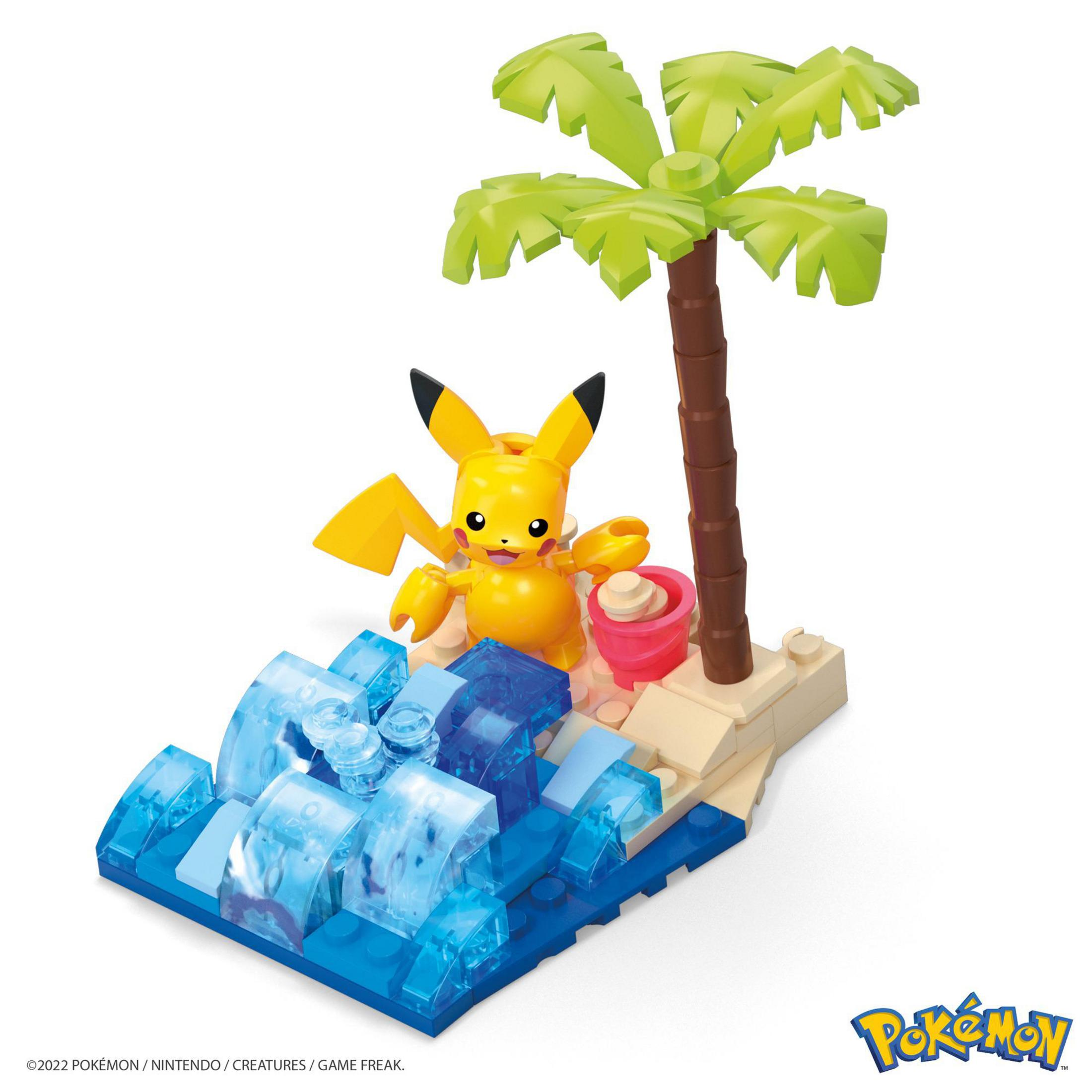 Pikachu Lego-Figur in einer Strandszene, mit Wasser, Sand, einer Palme und einem rosa Eimer.