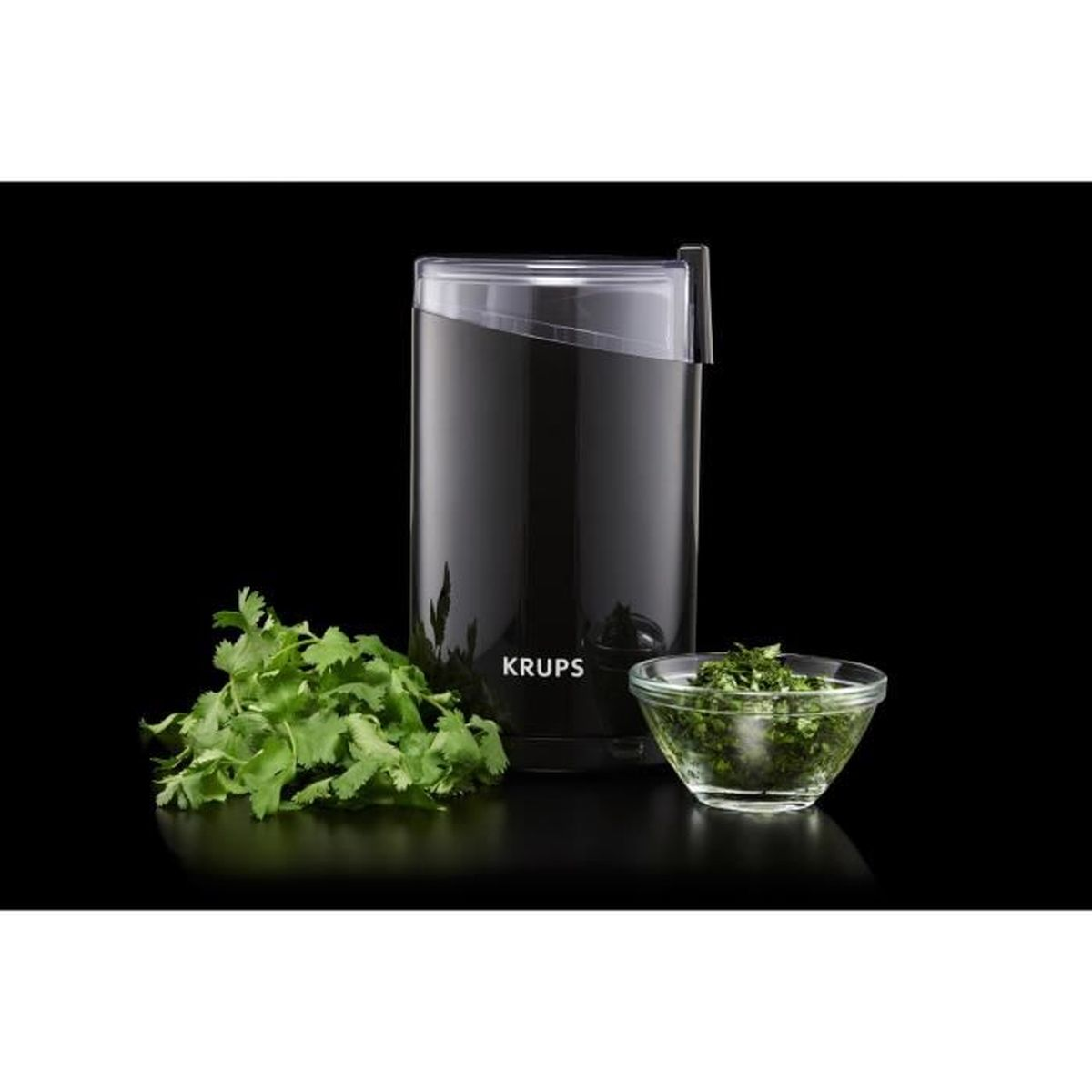 Zwarte Krups koffiemolen met gehakte koriander en kom op zwarte achtergrond.