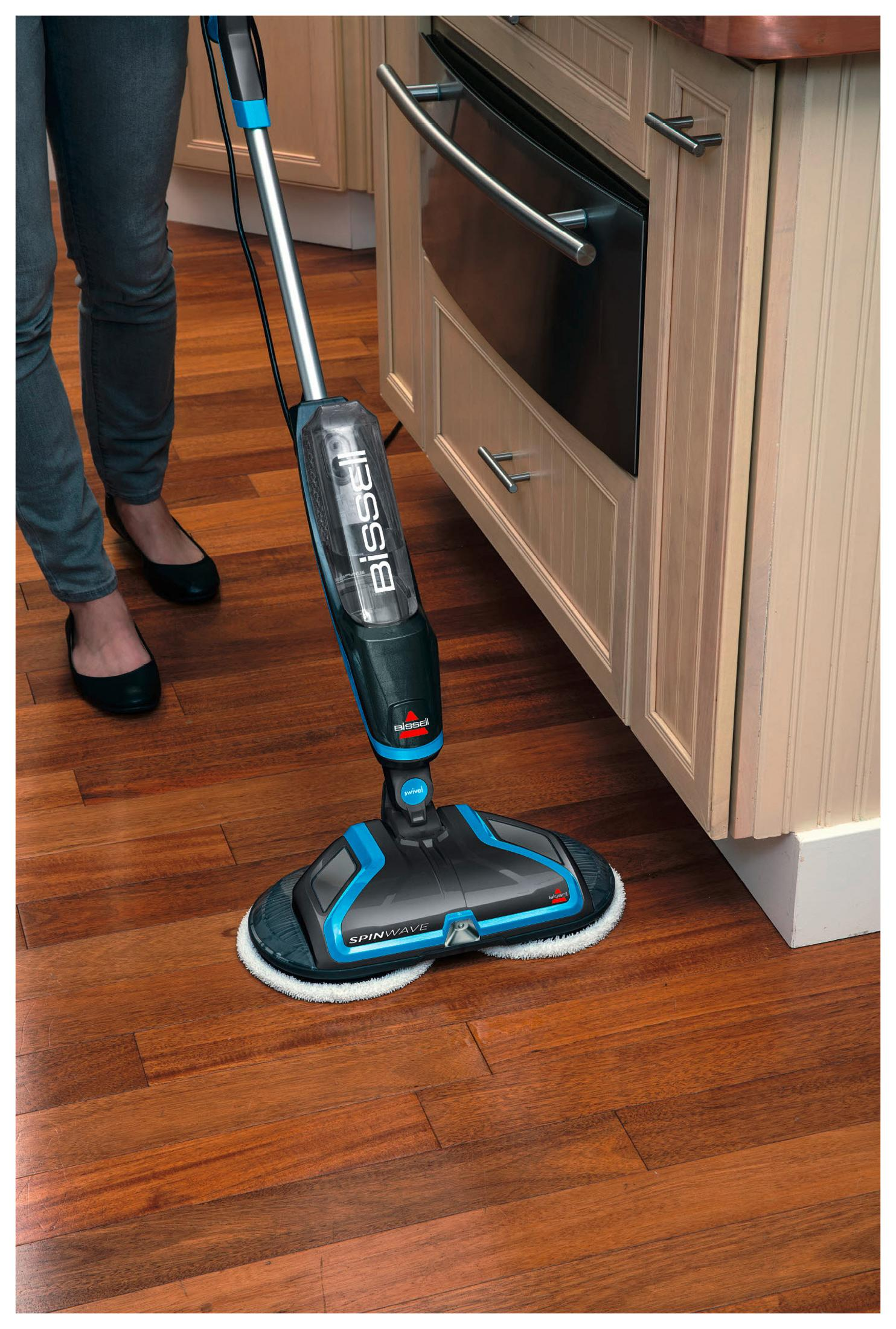 Person reinigt Holzboden mit Bissell Spinwave. Schwarzer und blauer Reiniger mit rotierenden Pads.