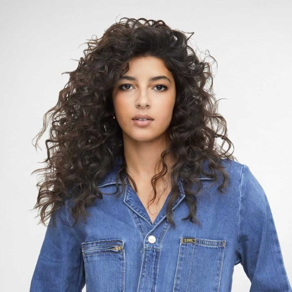 Kobieta z kręconymi, ciemnymi włosami w dżinsowej koszuli, patrząca w kamerę.