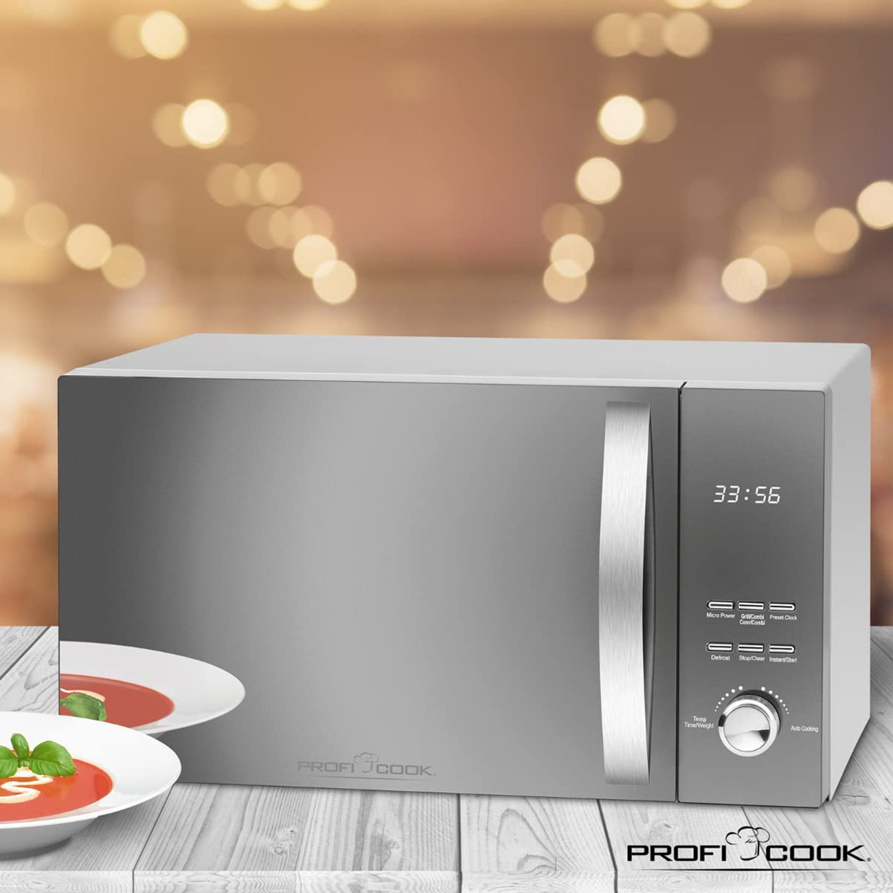 Srebrna kuchenka mikrofalowa na drewnianym stole. Dwie miski z zupą na pierwszym planie. Światła bokeh.