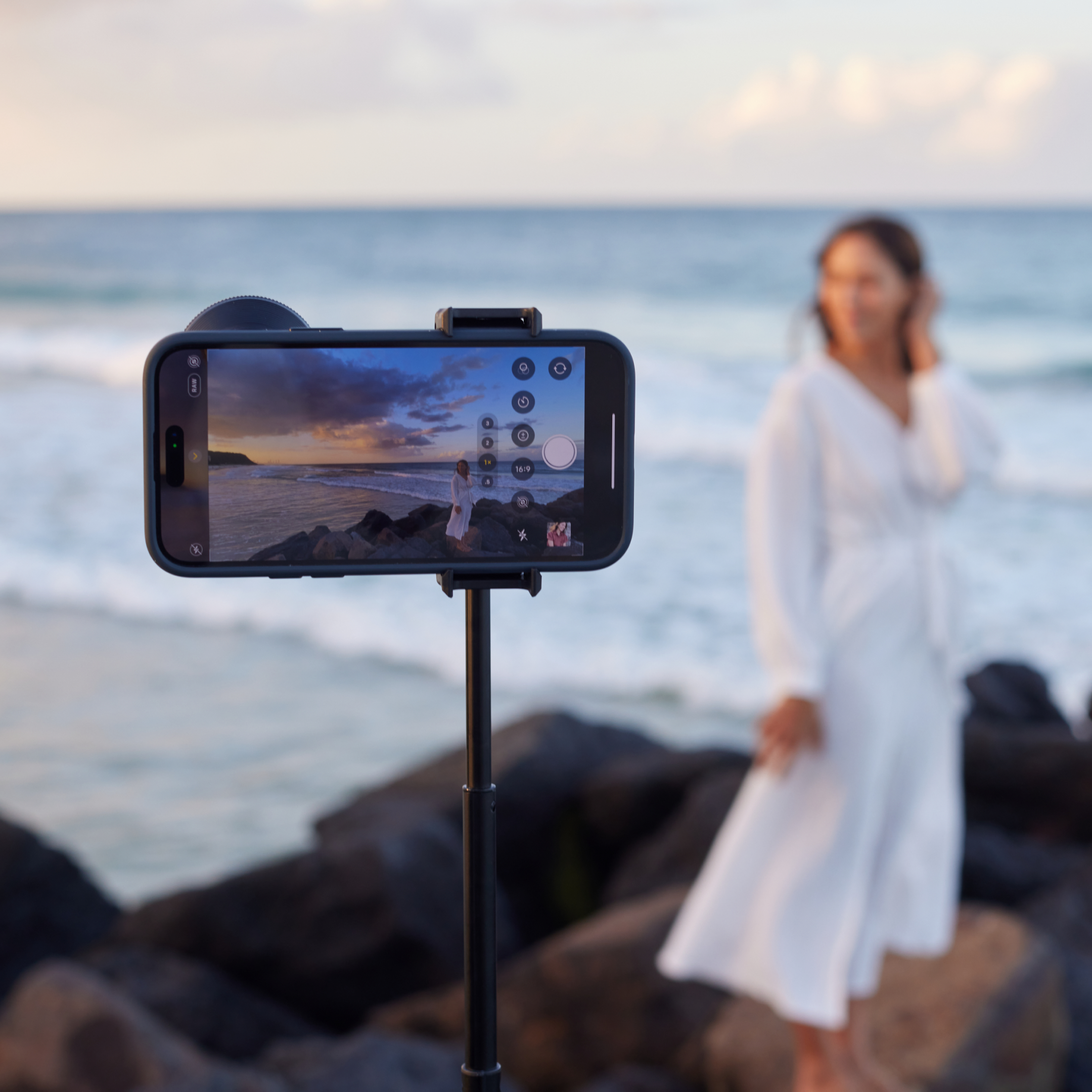 Person fotografiert Sonnenuntergang am Felsenstrand mit Handy.