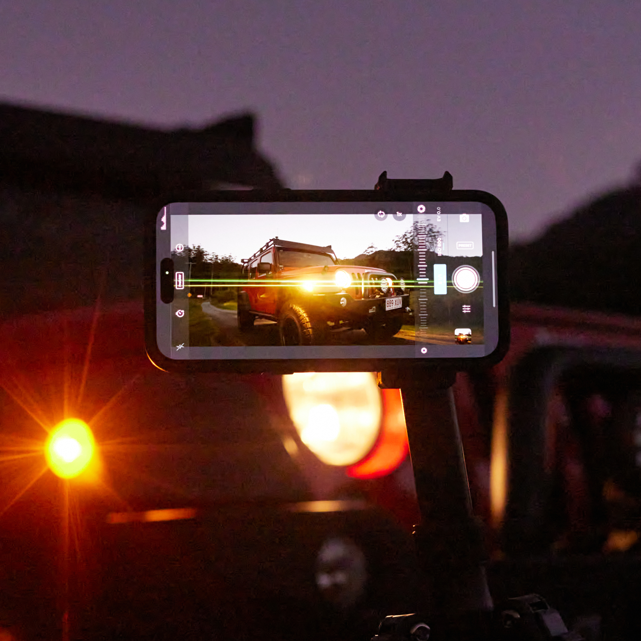 Smartphone filmt einen roten Jeep in der Abenddämmerung, mit Autoscheinwerfer und Benutzeroberfläche.