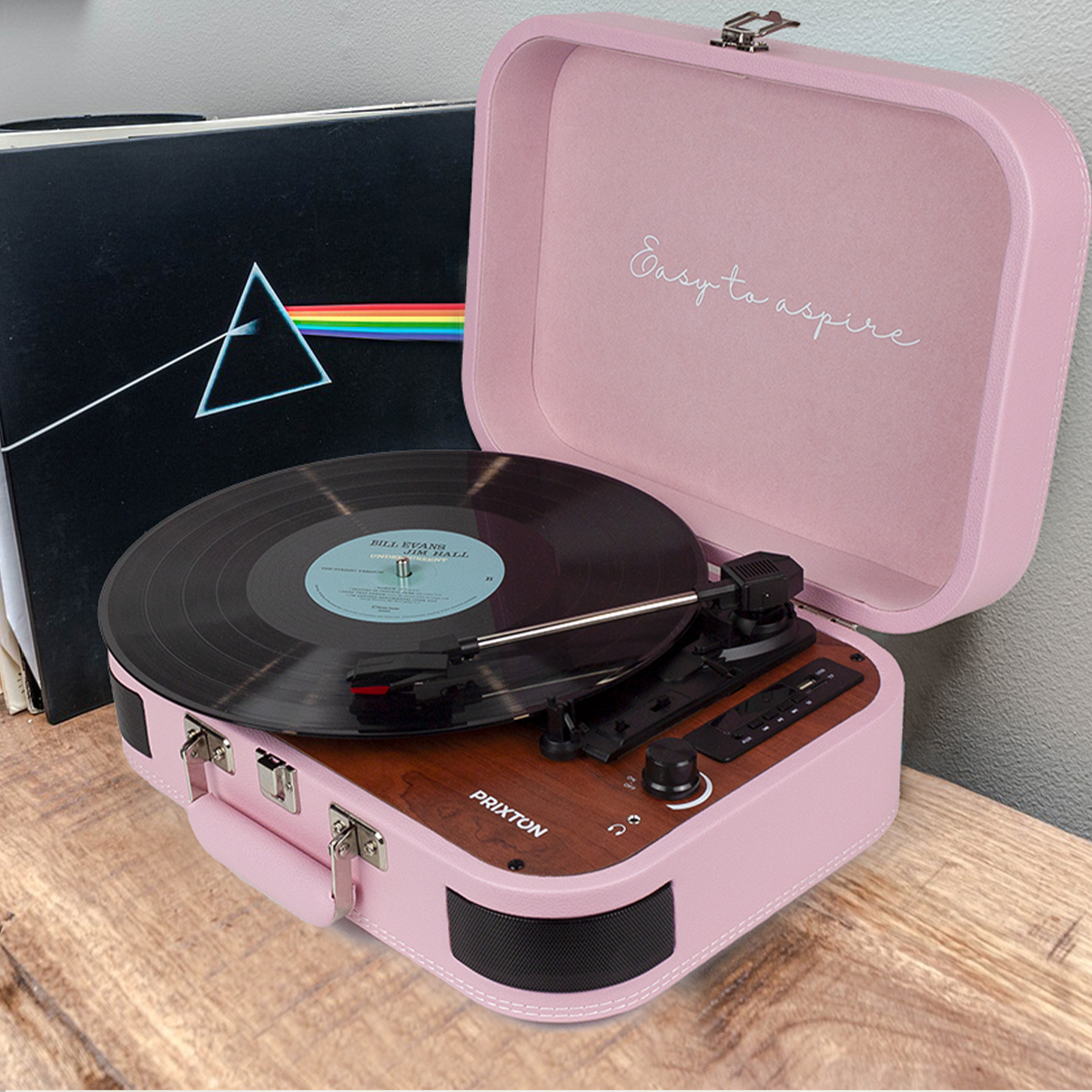 Różowy gramofon stoi na drewnie. Płyta winylowa się obraca. Na pokrywie napis 'Easy to aspire'.