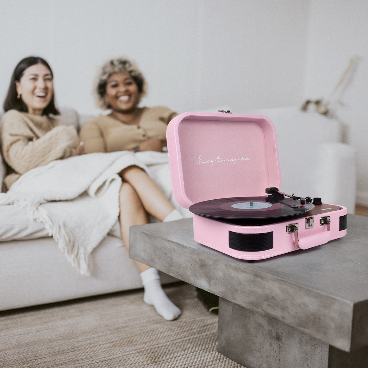 Różowy gramofon na stole z dwiema uśmiechniętymi kobietami w tle.