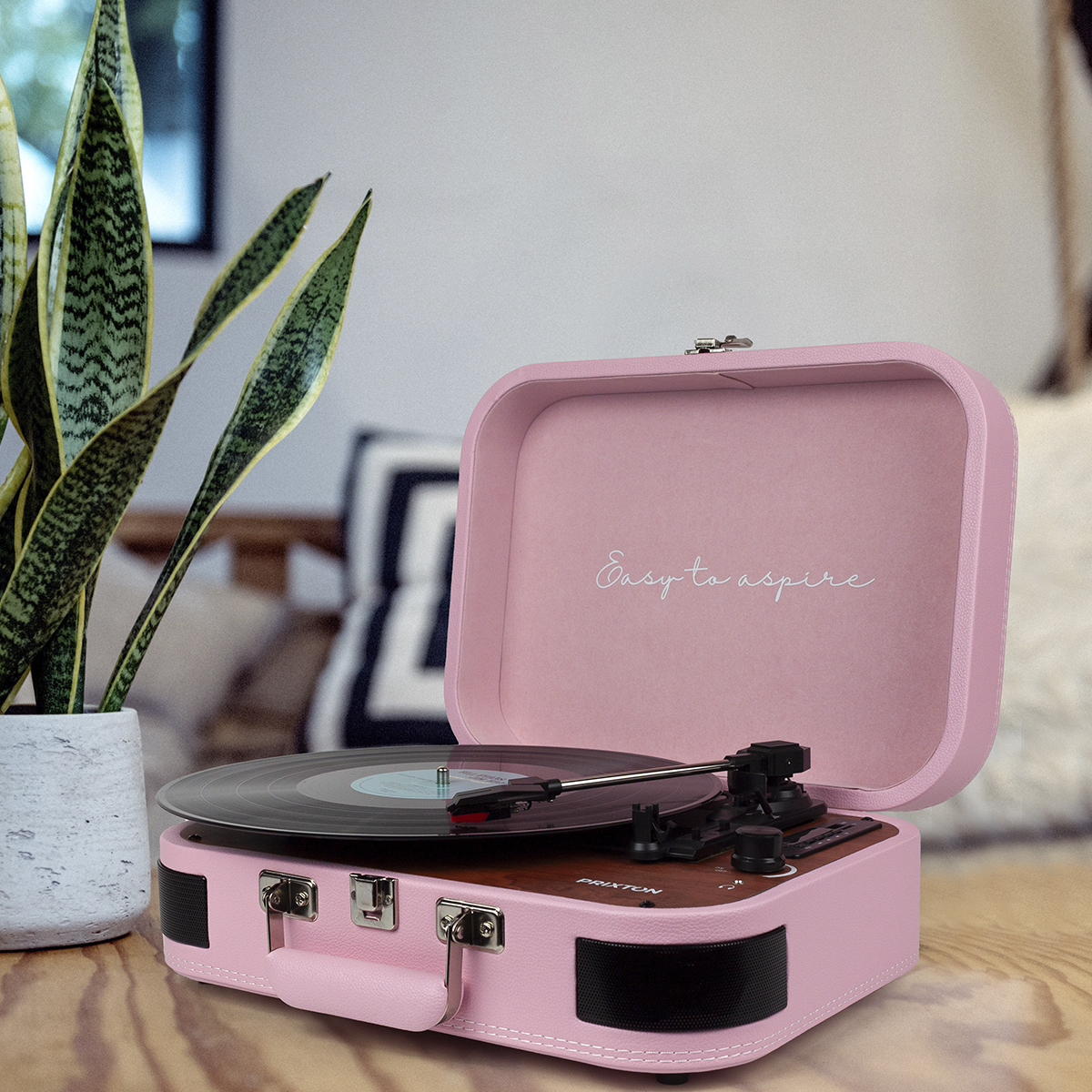 Różowy przenośny gramofon jest otwarty. Napis 'Easy to aspire'. Po lewej roślina w doniczce.