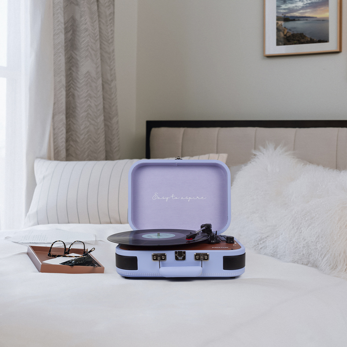 Zabytkowy gramofon stoi otwarty na łóżku. Taca ze szklankami i poduszką znajduje się na pierwszym planie.