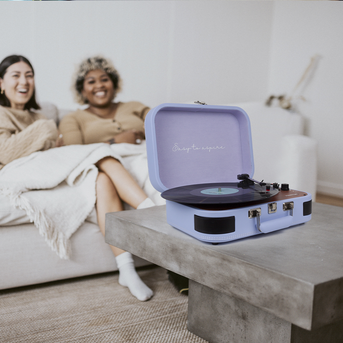 Dwie kobiety na kanapie obok gramofonu na stole. Gramofon jest jasnoniebieski.