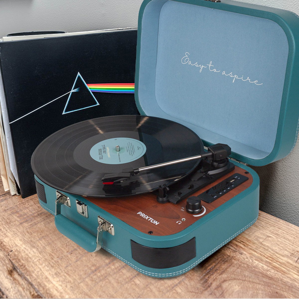 Zabytkowy gramofon z turkusową obudową, płytami i akcesoriami, na drewnianej powierzchni.