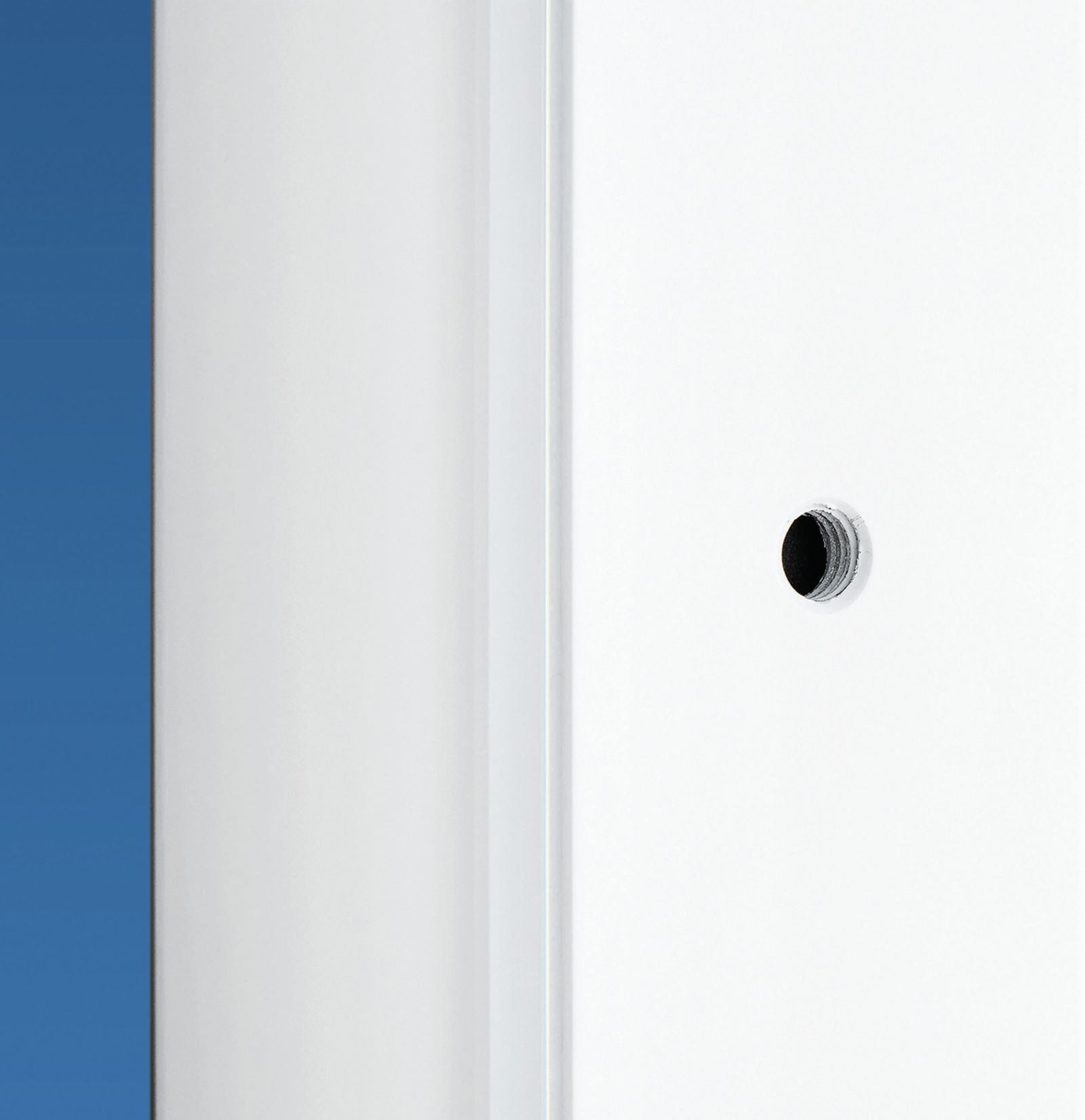 Biała ściana z małym, ciemnym otworem na tle niebieskiego tła.