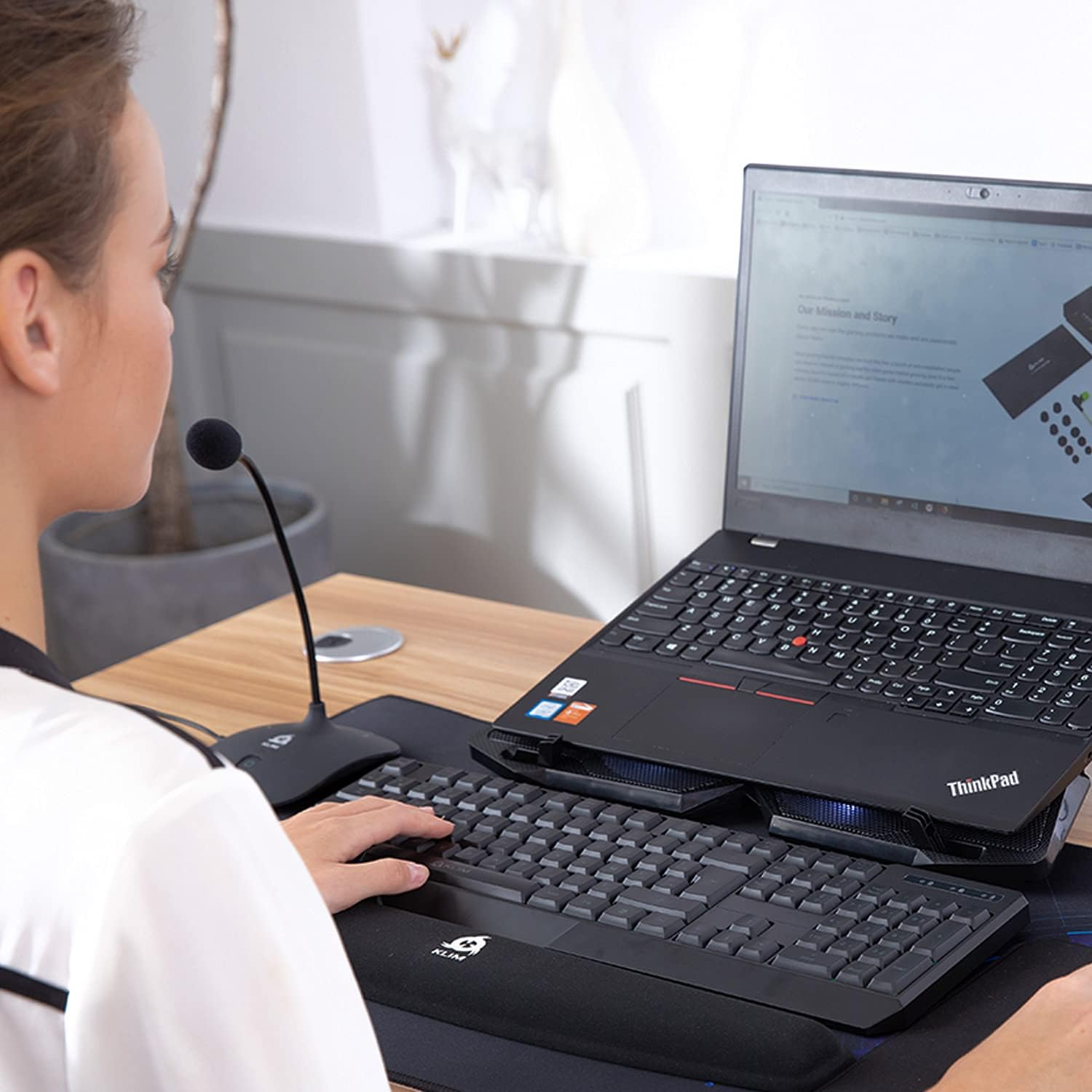 Frau benutzt Laptop, Tastatur, Maus und Mikrofon auf einem Schreibtisch.