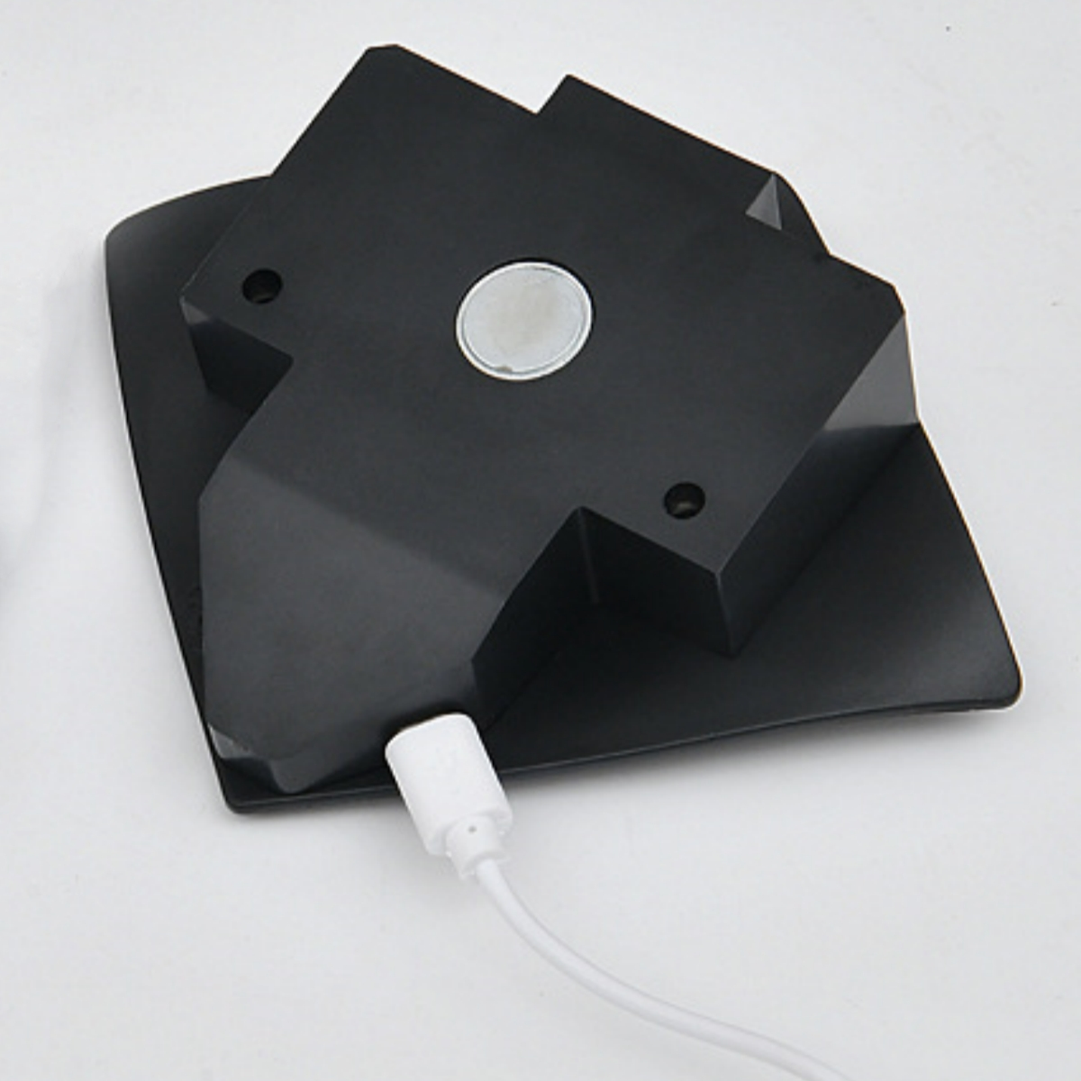 Schwarzes Ladegerät mit weißem Kabel. Das Gerät befindet sich auf einer weißen Oberfläche.