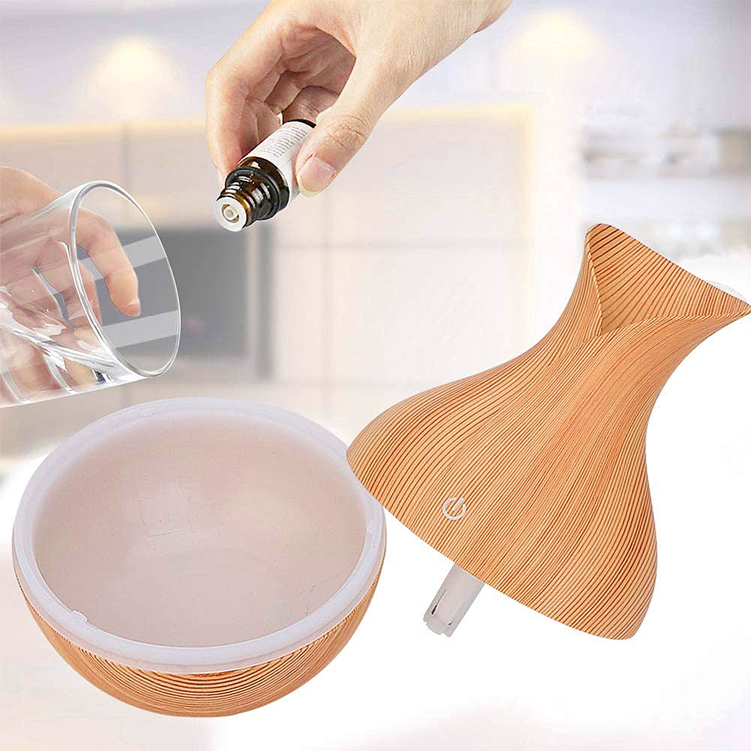 Botella de aceite esencial vertiendo en un vaso de agua, con un difusor de diseño de madera al lado.