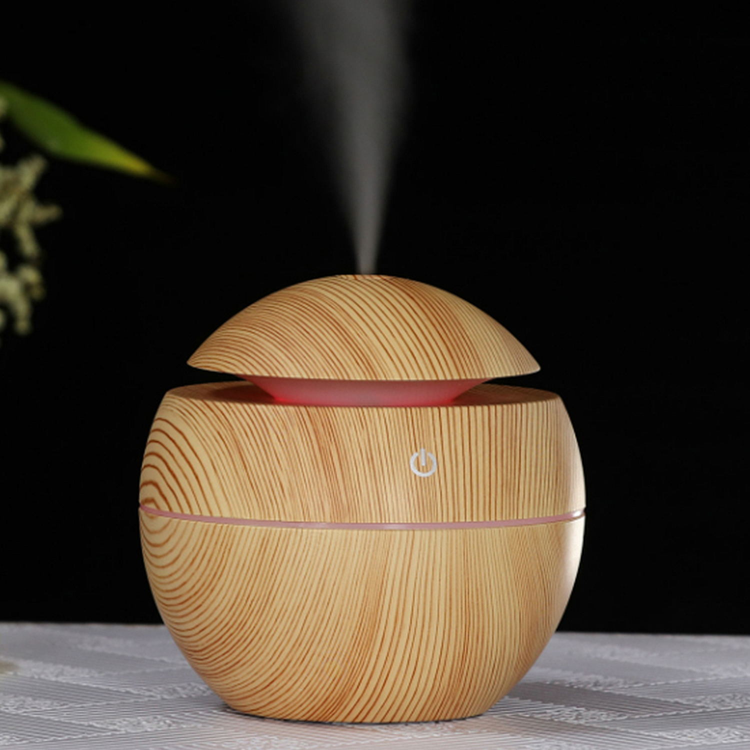Un difusor con patrón de vetas de madera. Es redondo, con un botón y una luz. Fondo negro.