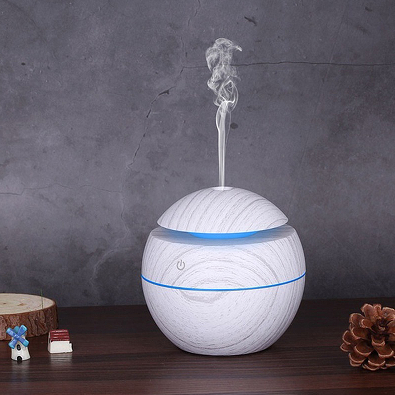 Un difusor de aroma blanco y veteado de madera con vapor saliendo y pequeñas decoraciones.
