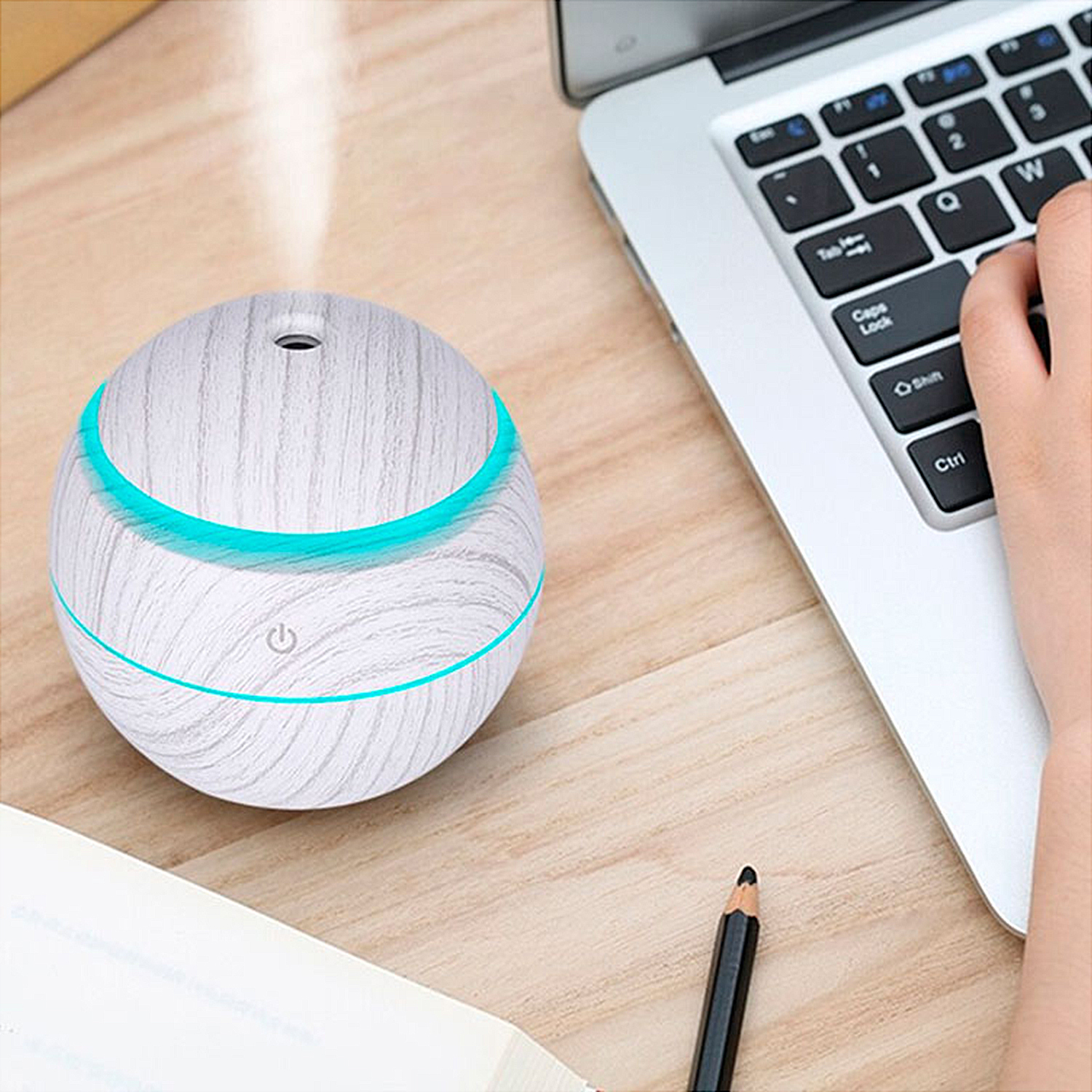 Un humidificador blanco y con vetas de madera emite vapor. Se encuentra sobre una mesa con una computadora portátil y un lápiz cerca.