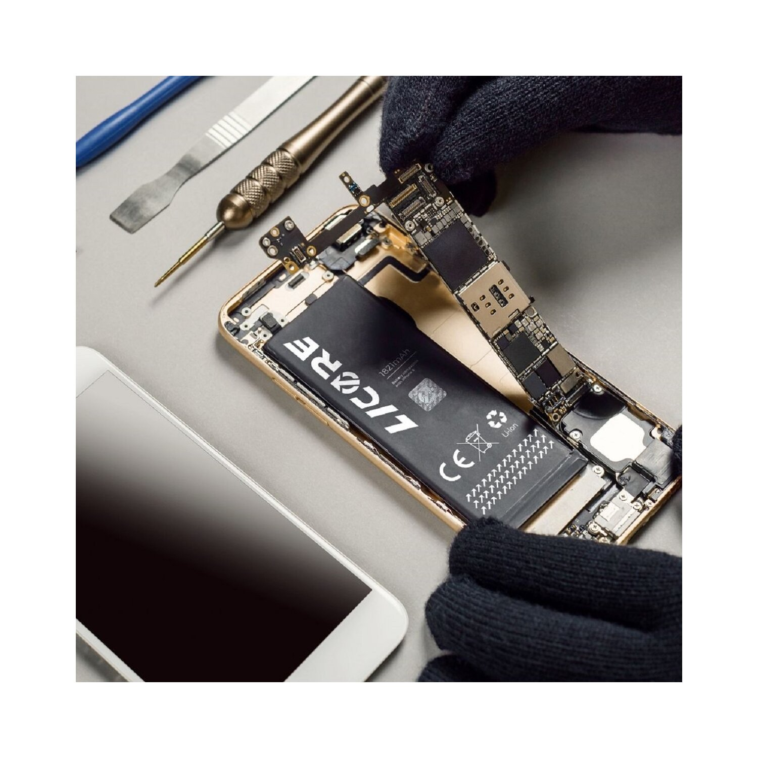 Zerlegtes Telefon mit sichtbarem Akku und Leiterplatten, Werkzeuge und ein Telefon auf grauer Oberfläche.